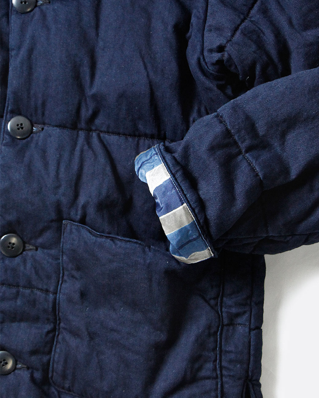 A close up of the cuffed sleeves of a navy quilted denim jacket with a button front. Shown from the front