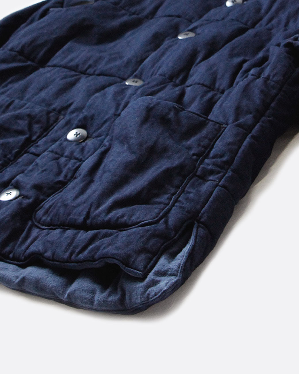 A close up from the front of a pocket on a navy quilted denim jacket with button closure and two front pockets.