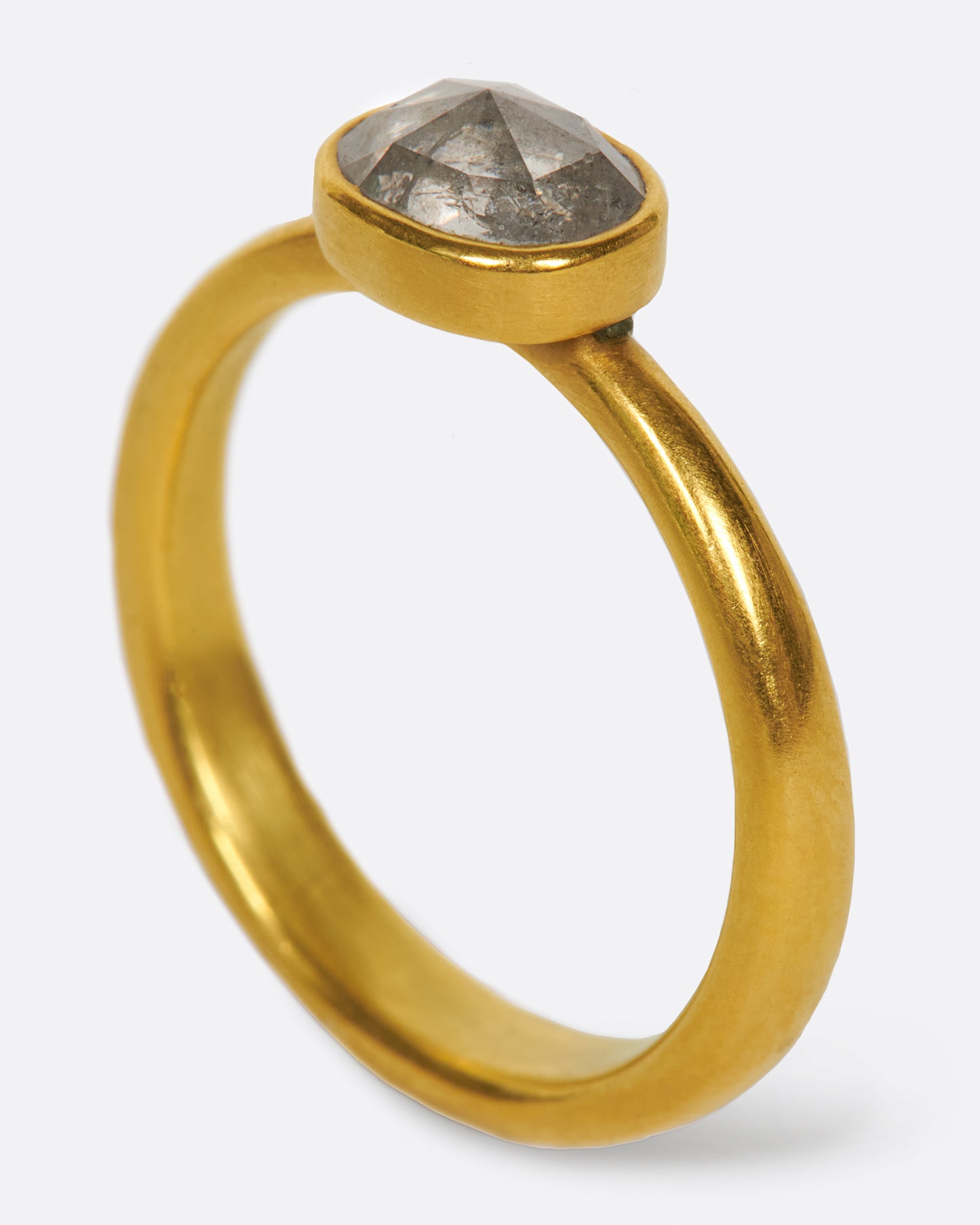 A pale grey, rose cut, oval diamond. Set horizontally on a simple, yellow gold band. Shown standing up from the side.