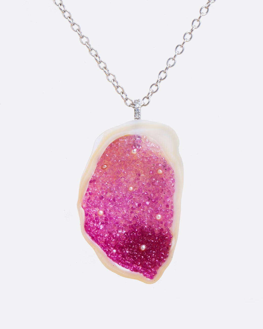 A large freshwater souffle pearl carved out and lined with ombre pink sapphires and seed pearls. It has a pave diamond lined bail and white gold cable chain. Shown from the front.