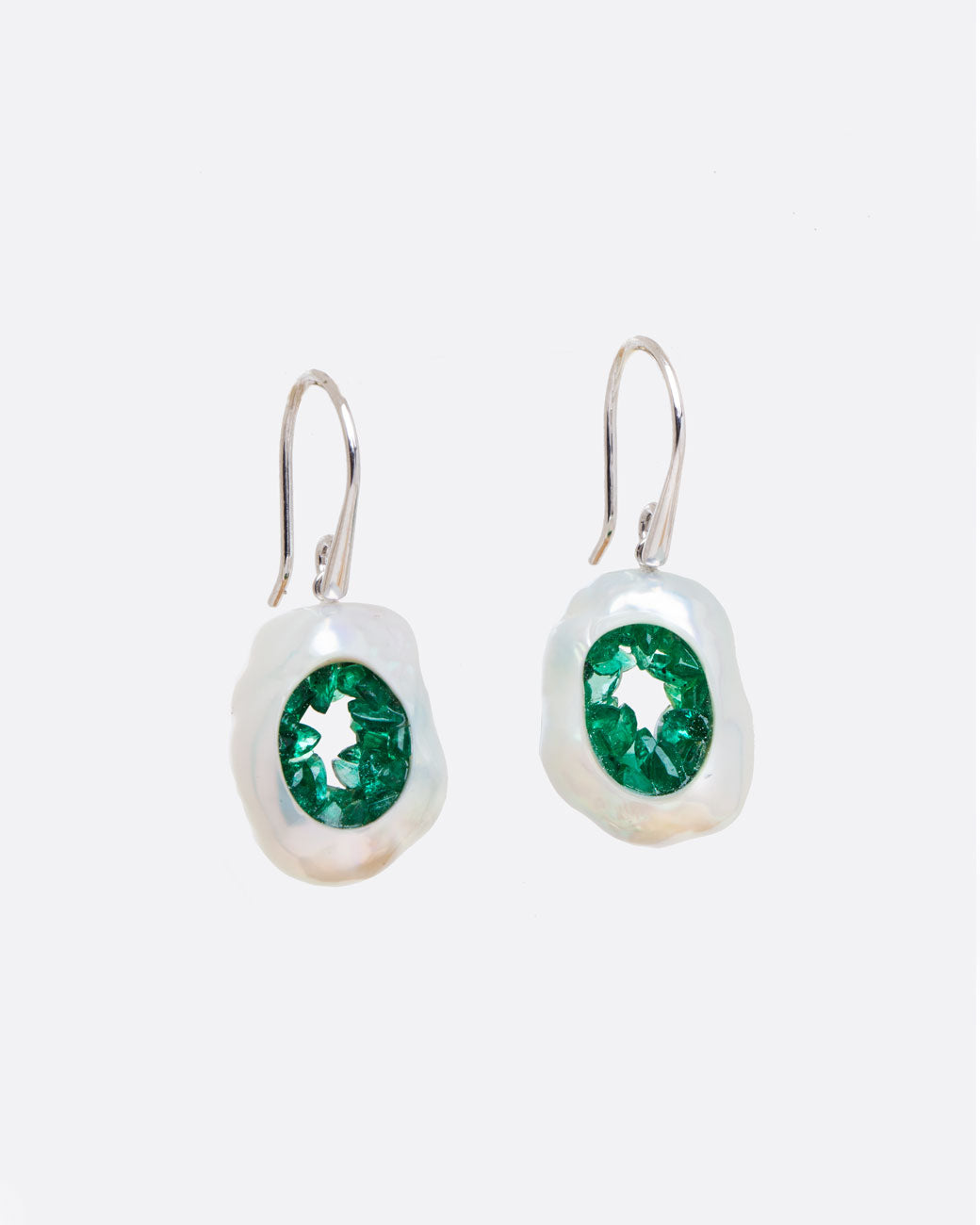 A pair of dangle earrings with hollow pearls lined with emeralds and white gold ear hooks. Shown from the front.