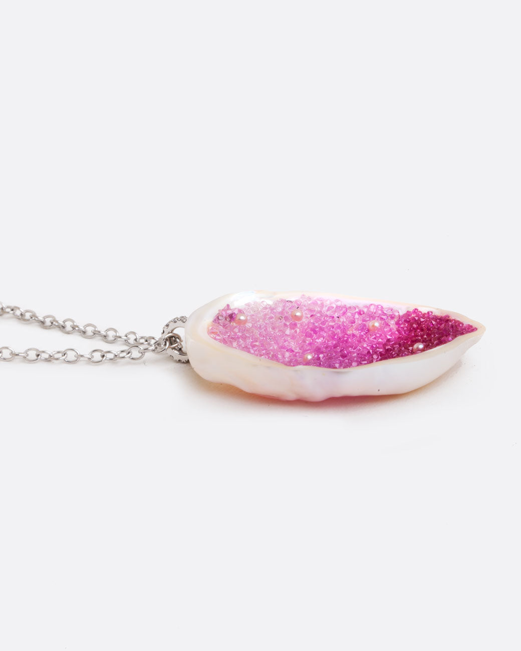 A large freshwater souffle pearl carved out and lined with ombre pink sapphires and seed pearls. It has a pave diamond lined bail and white gold cable chain. Shown from the side.