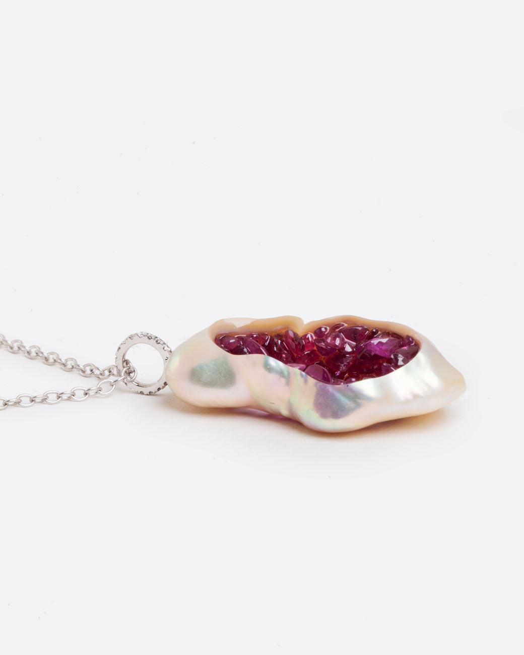 A large soufflé pearl open in the center and filled with pearls and amethysts, hanging from a white gold cable chain and a diamond bail. Shown lying flat closed from the side.