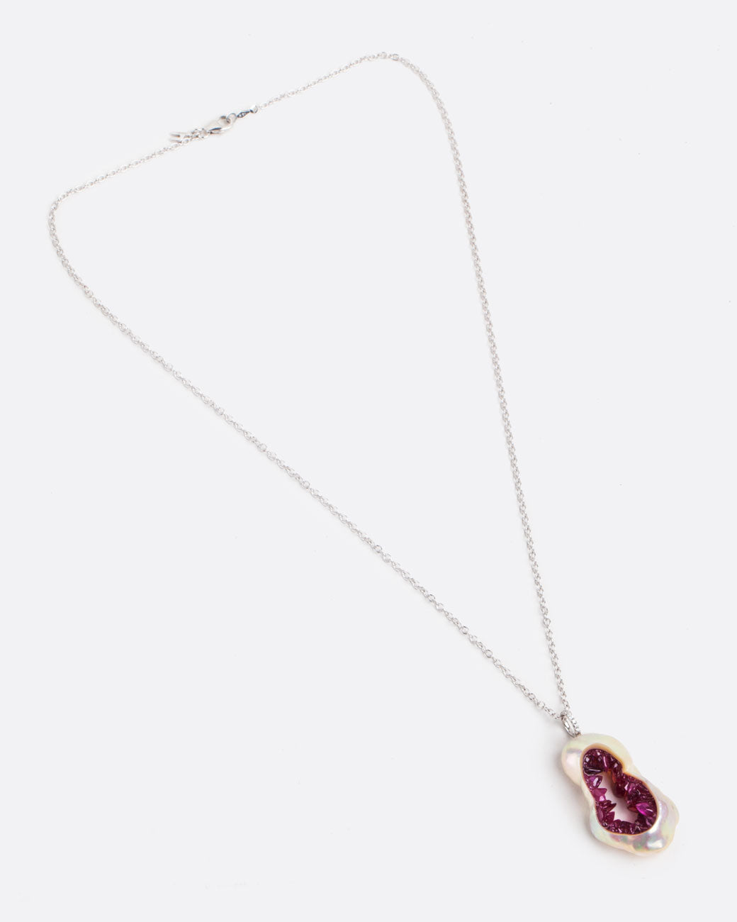 A large soufflé pearl open in the center and filled with pearls and amethysts, hanging from a white gold cable chain and a diamond bail. Shown lying flat closed from the front.