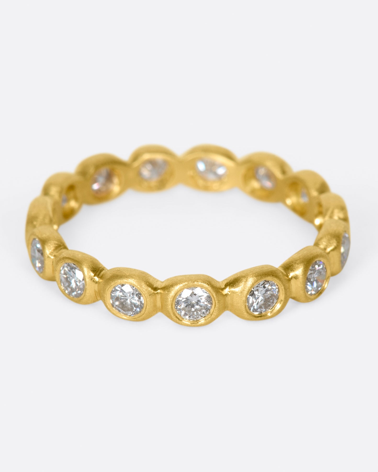 A yellow gold eternity band of bezel set white diamonds. Shown from the front.