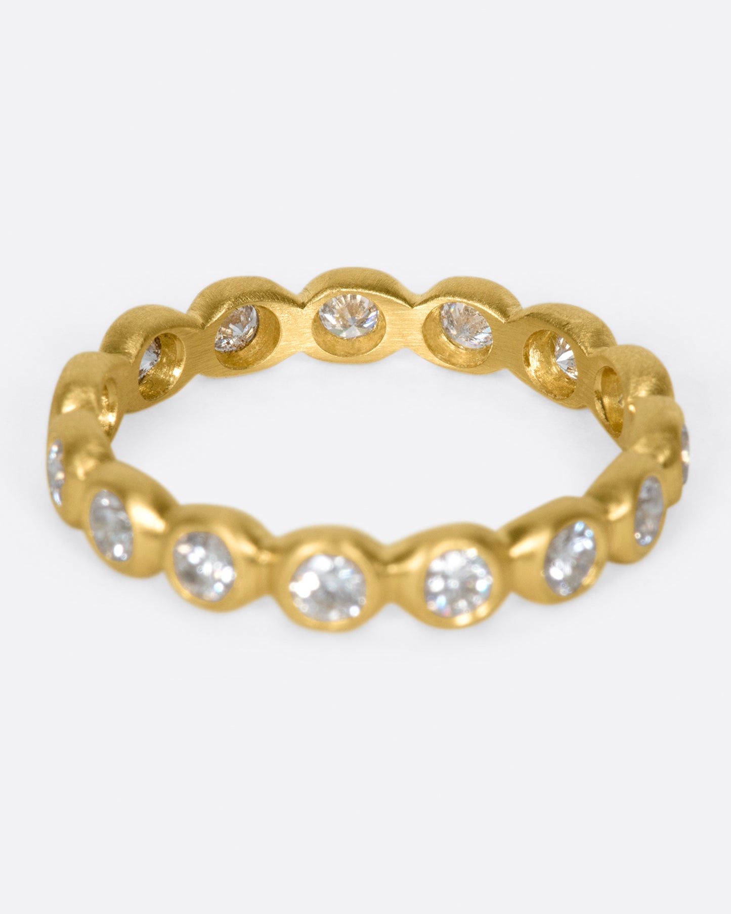 A yellow gold eternity band of bezel set white diamonds. Shown from the front.