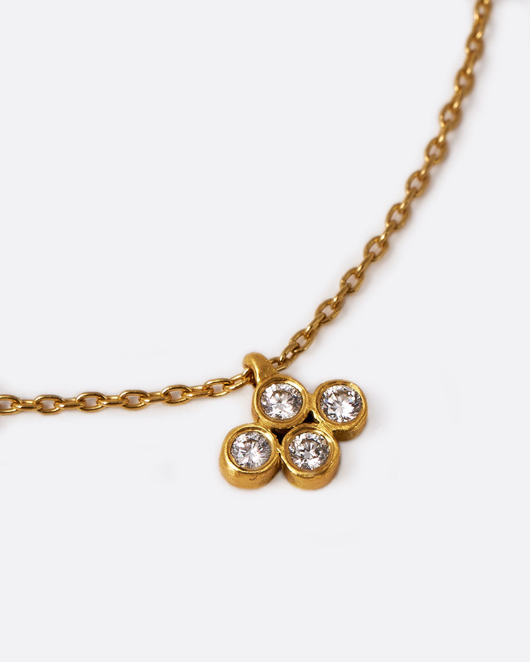 A yellow gold cable chain necklace with a pendant of four two point diamonds. Shown lying flat at a diagonal from the front.