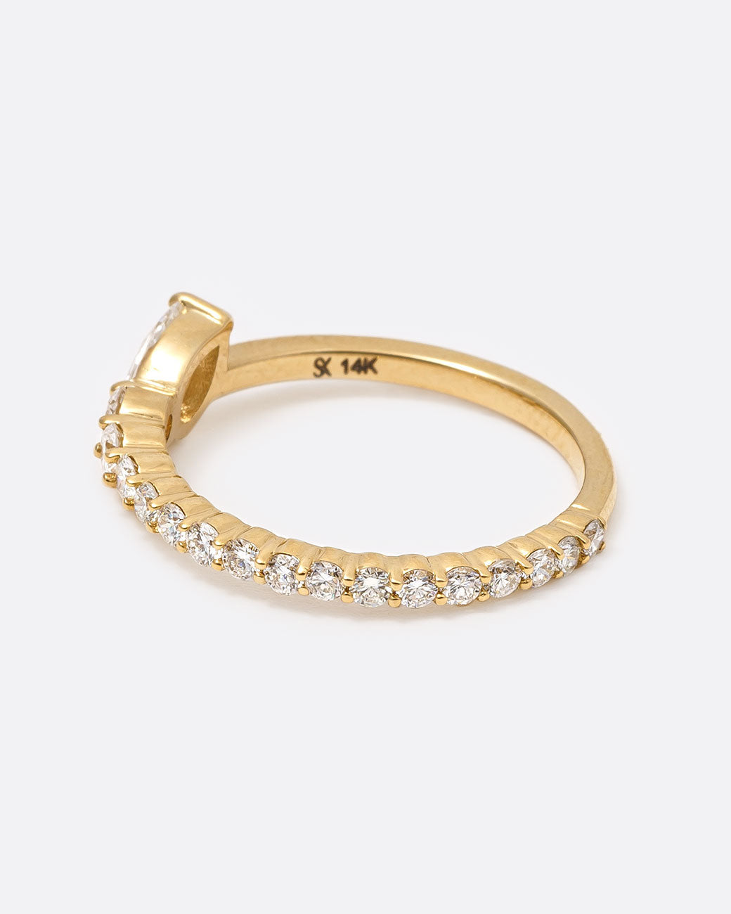 14k yellow gold ring with graduated white diamonds halfway around and one pear shaped white diamond by Selin Kent, shown from the side.