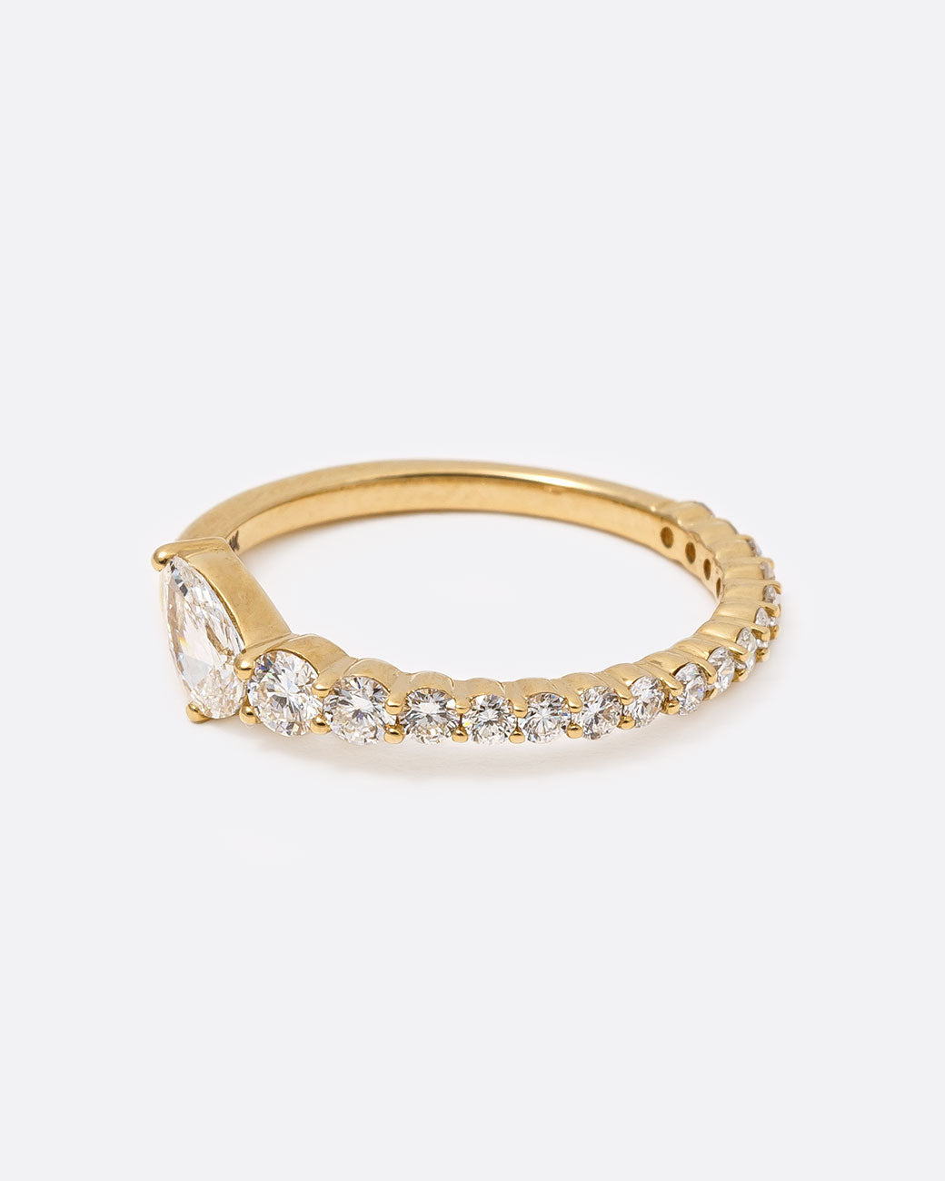 14k yellow gold ring with graduated white diamonds halfway around and one pear shaped white diamond by Selin Kent, shown from the side.