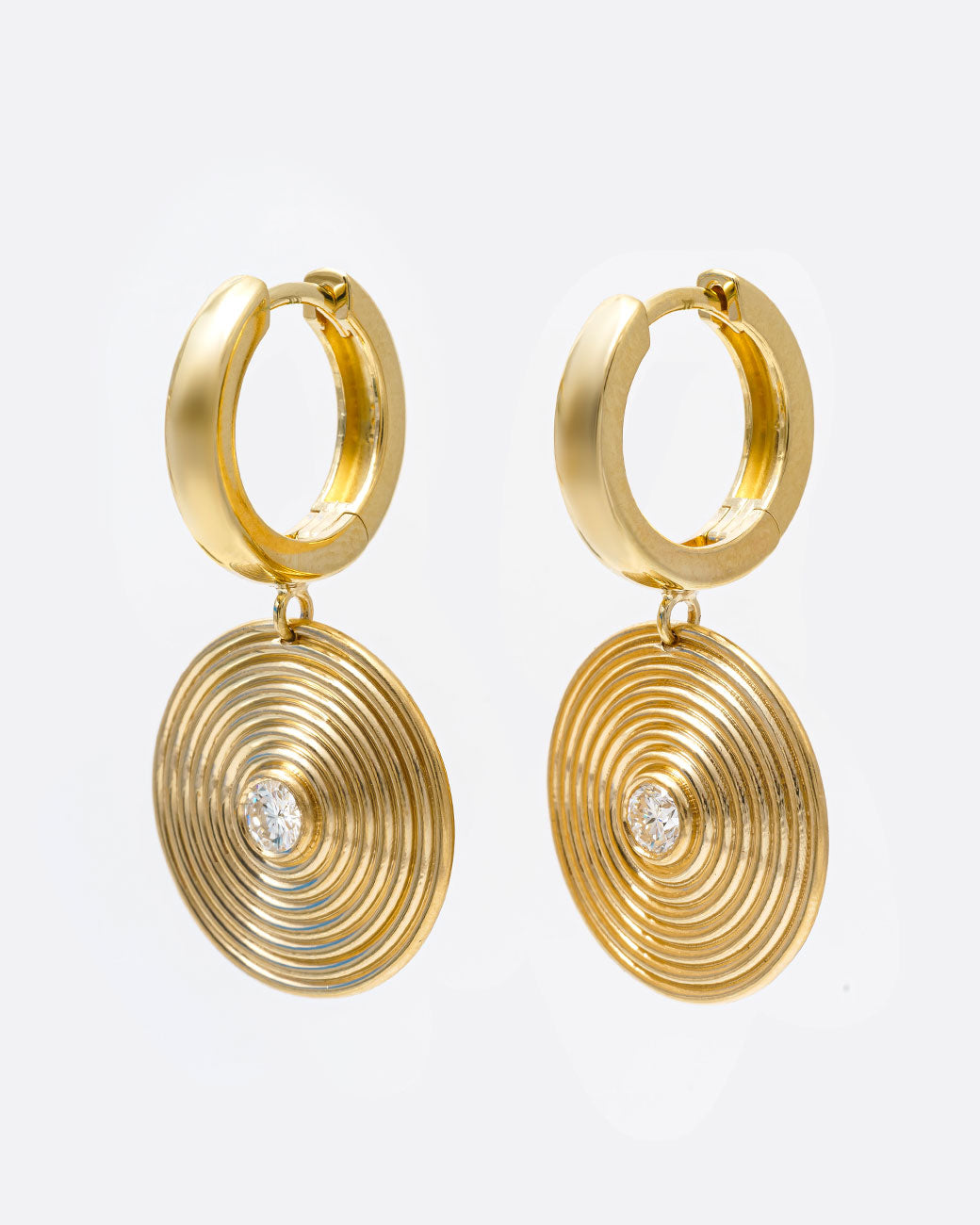 A pair of yellow gold hoop earrings with circular ribbed disc drops with white diamond centers, shown from the side.