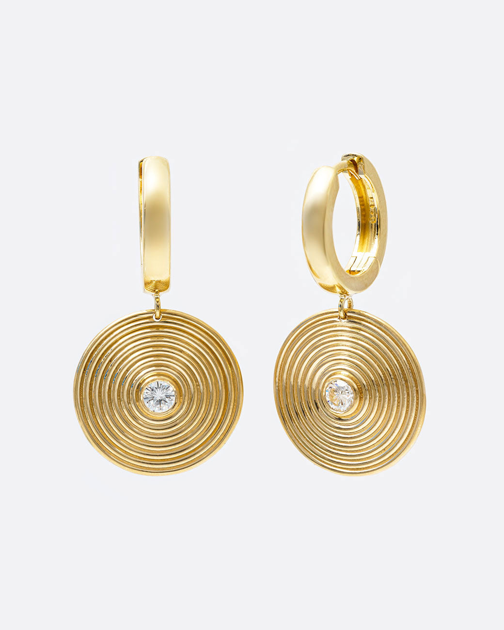 A pair of yellow gold hoop earrings with circular ribbed disc drops with white diamond centers. One earring is shown from the front, the other is shown from the side.
