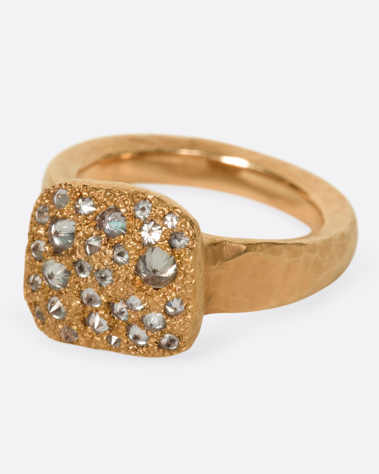 A hammered, hefty rose gold ring with inverted diamonds scattered across its rectangular face. Shown at an angle from the front.