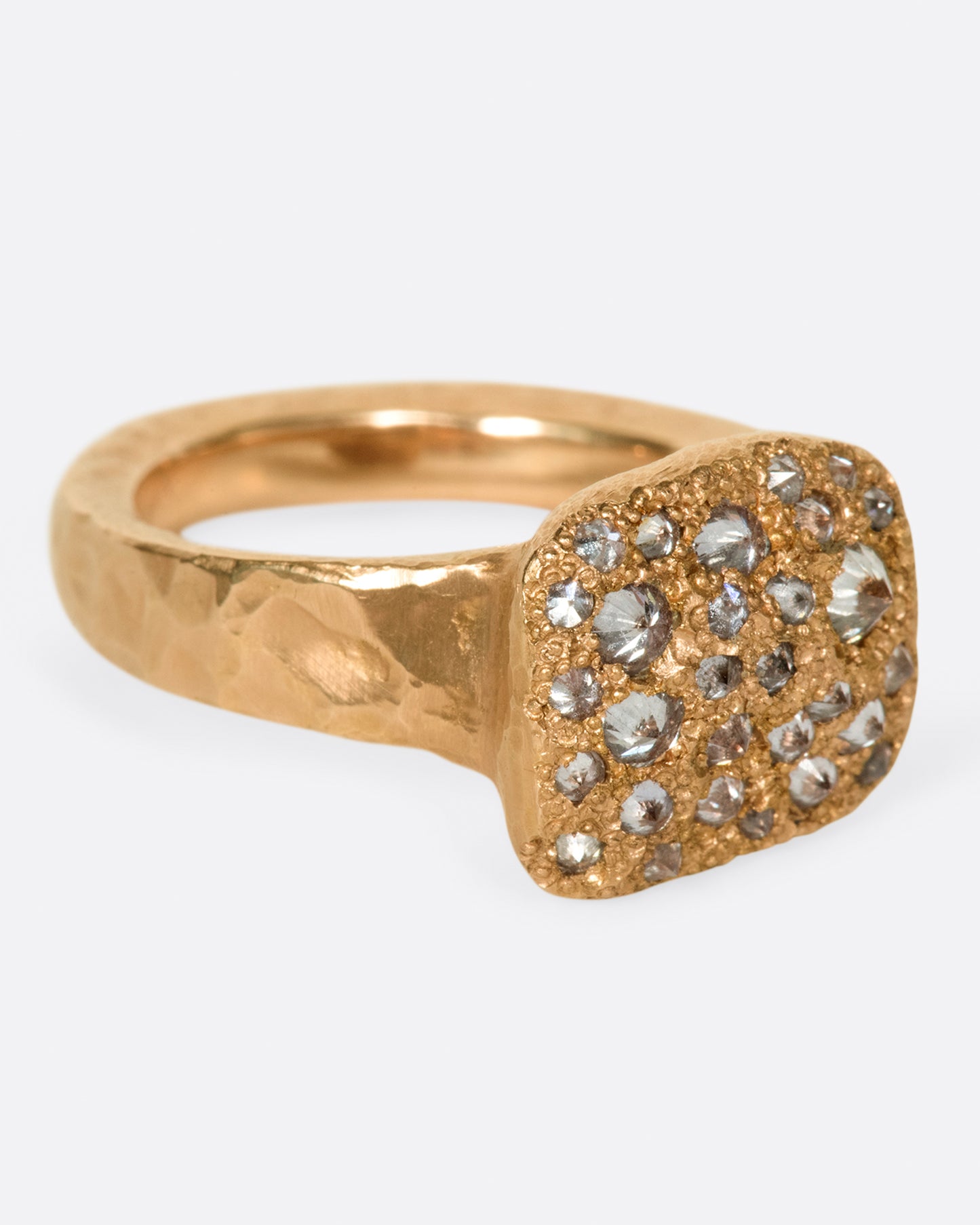 A hammered, hefty rose gold ring with inverted diamonds scattered across its rectangular face. Shown from the side.