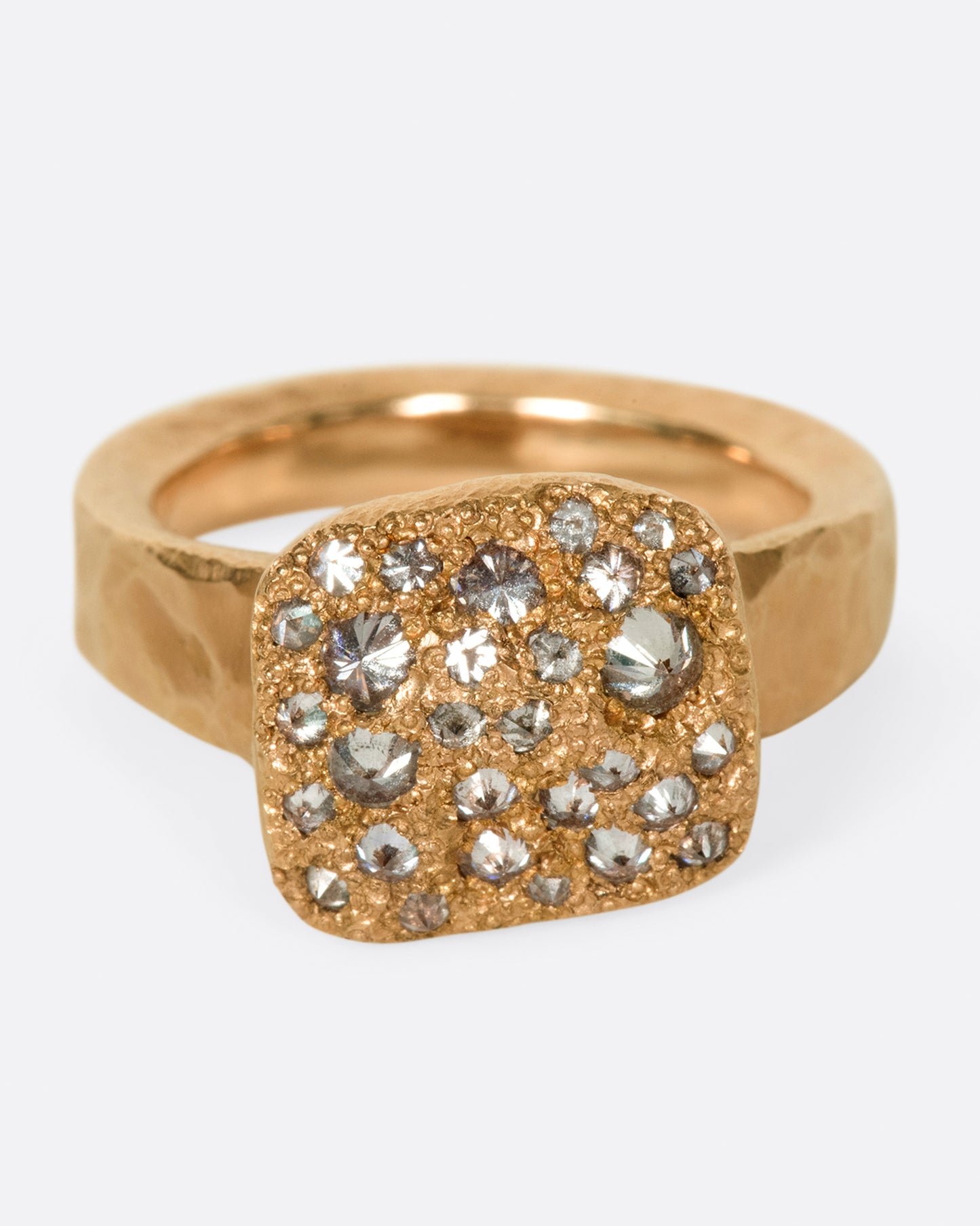A hammered, hefty rose gold ring with inverted diamonds scattered across its rectangular face. Shown from the front.