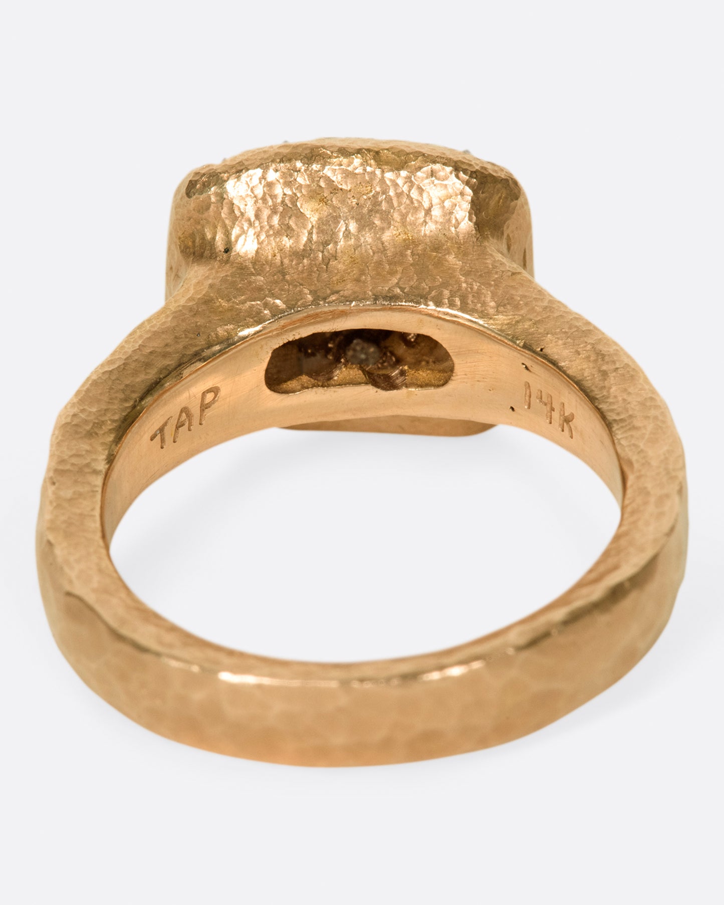 A hammered, hefty rose gold ring with inverted diamonds scattered across its rectangular face. Shown from the back.