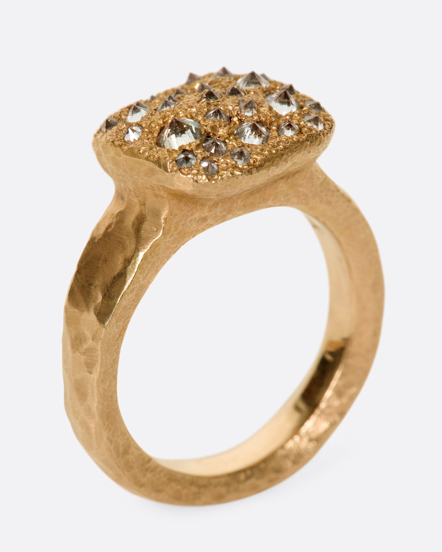 A hammered, hefty rose gold ring with inverted diamonds scattered across its rectangular face. Shown standing up at an angle.
