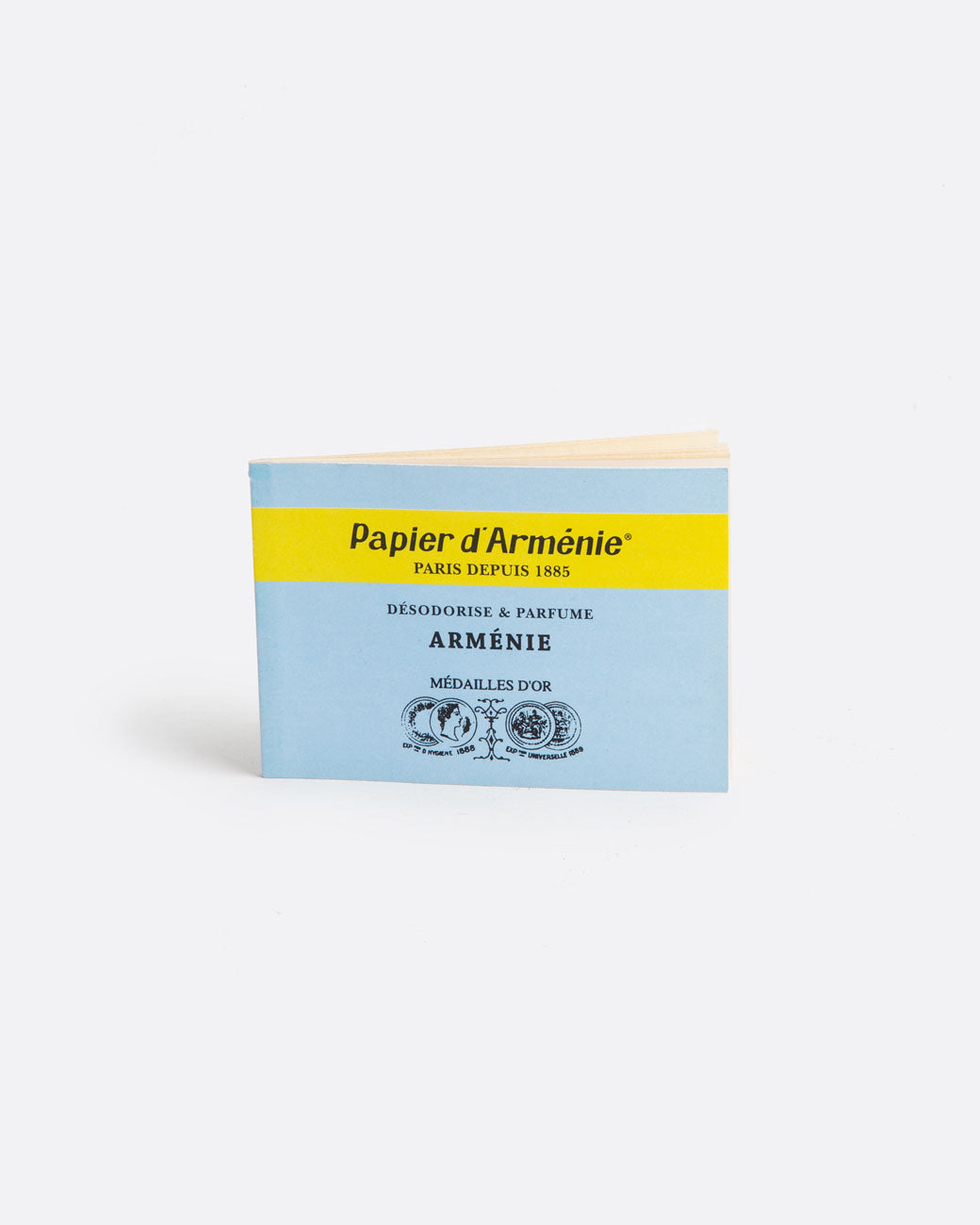 A light blue and yellow booklet of paper incense. The front reads: 'Paper d'Arménie PARIS DEPUIS 1885 DÉSODORISE & PARFUME ARMÉNIE MÉDAILLE D'OR' and has medallion imagery at the bottom. Shown standing up from the front.
