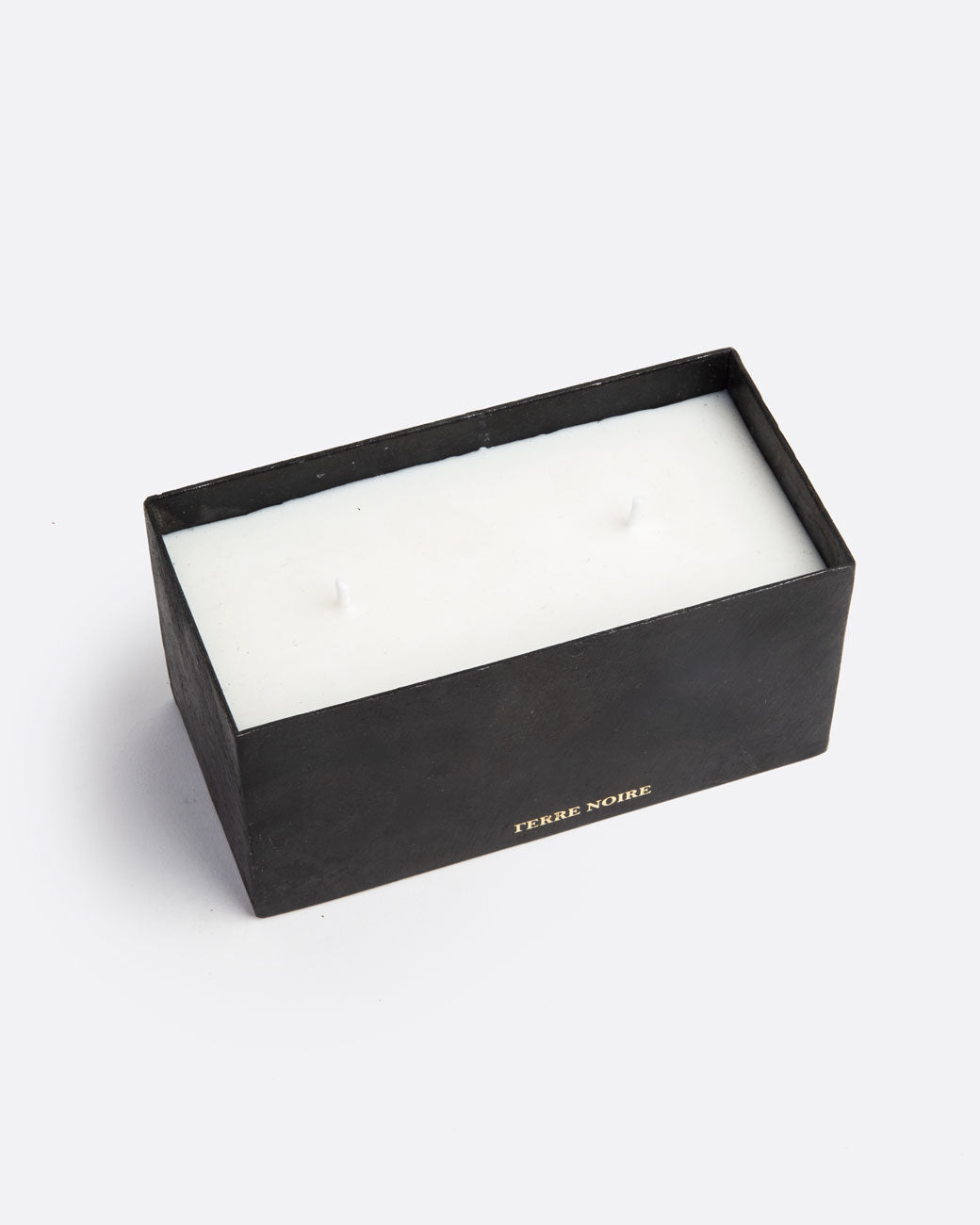 A white block candle with two wicks in a rectangular black container with TERRE NOIRE in gold lettering at the base. Shown from the top.