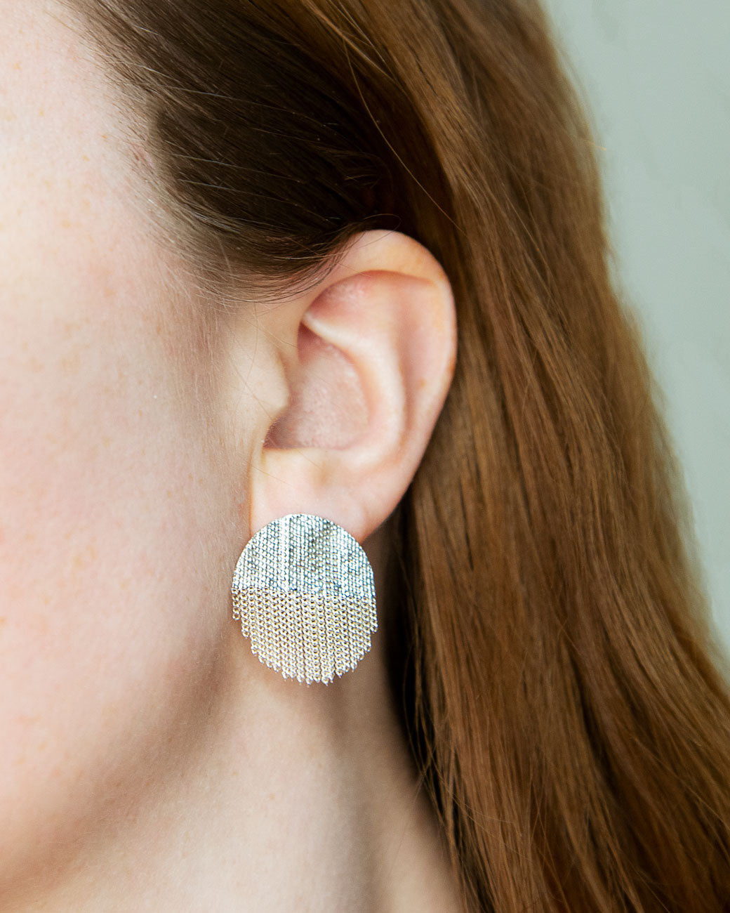 A pair of silver earrings with soldered half circle tops and chain fringe half circle bottoms. Shown from the front on a person.