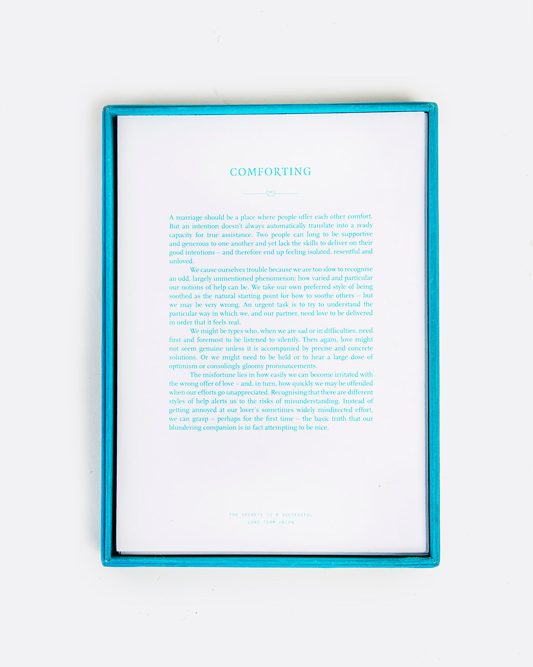 A turquoise box open, displaying a white card with turquoise lettering. Shown lying flat from the top.