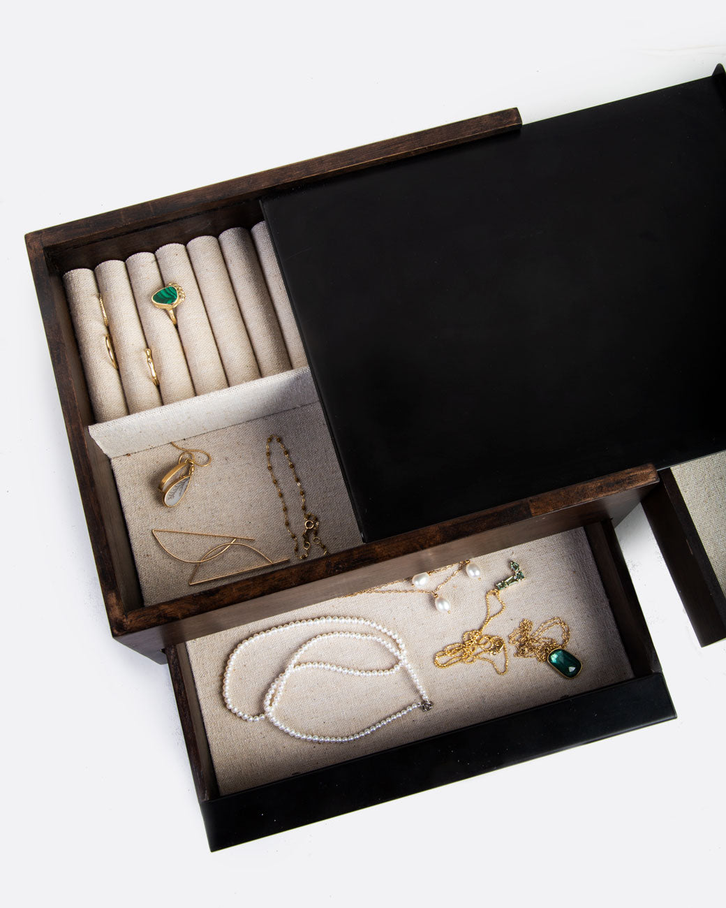 A wooden jewelry box with metal details and a tan fabric lined interior. There are three compartments, one with spots for rings and two sliding drawers. Shown with jewelry in it from the top.