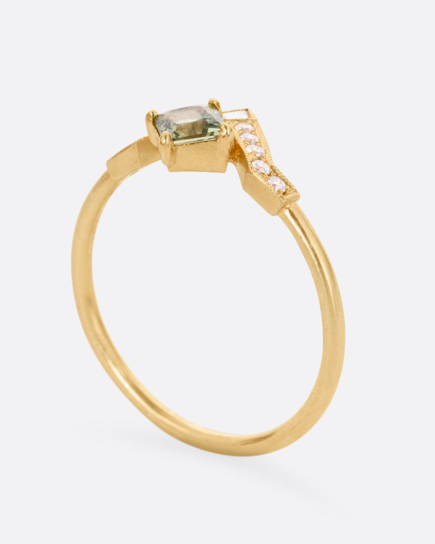 A yellow gold ring with a diamond arch and green sapphire. Shown from the side standing up.