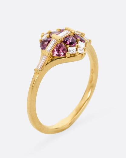 A yellow gold ring with a row of baguette diamonds passing through a cluster of trillion cut garnets and diamond accents. Shown from the side standing up.