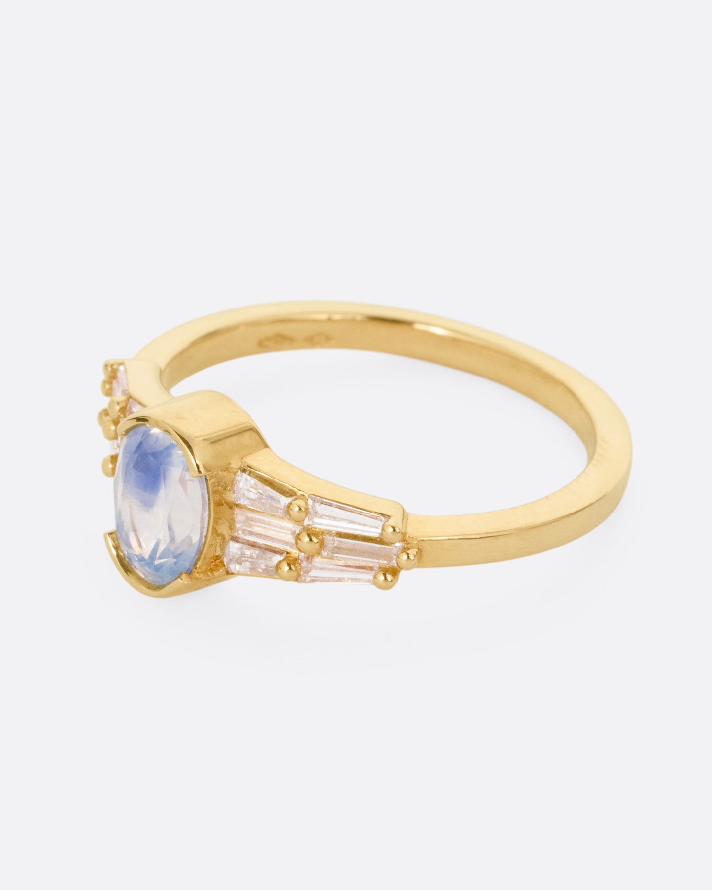 A yellow gold ring with stacked baguette diamonds and a bezel set sapphire, shown from the side.