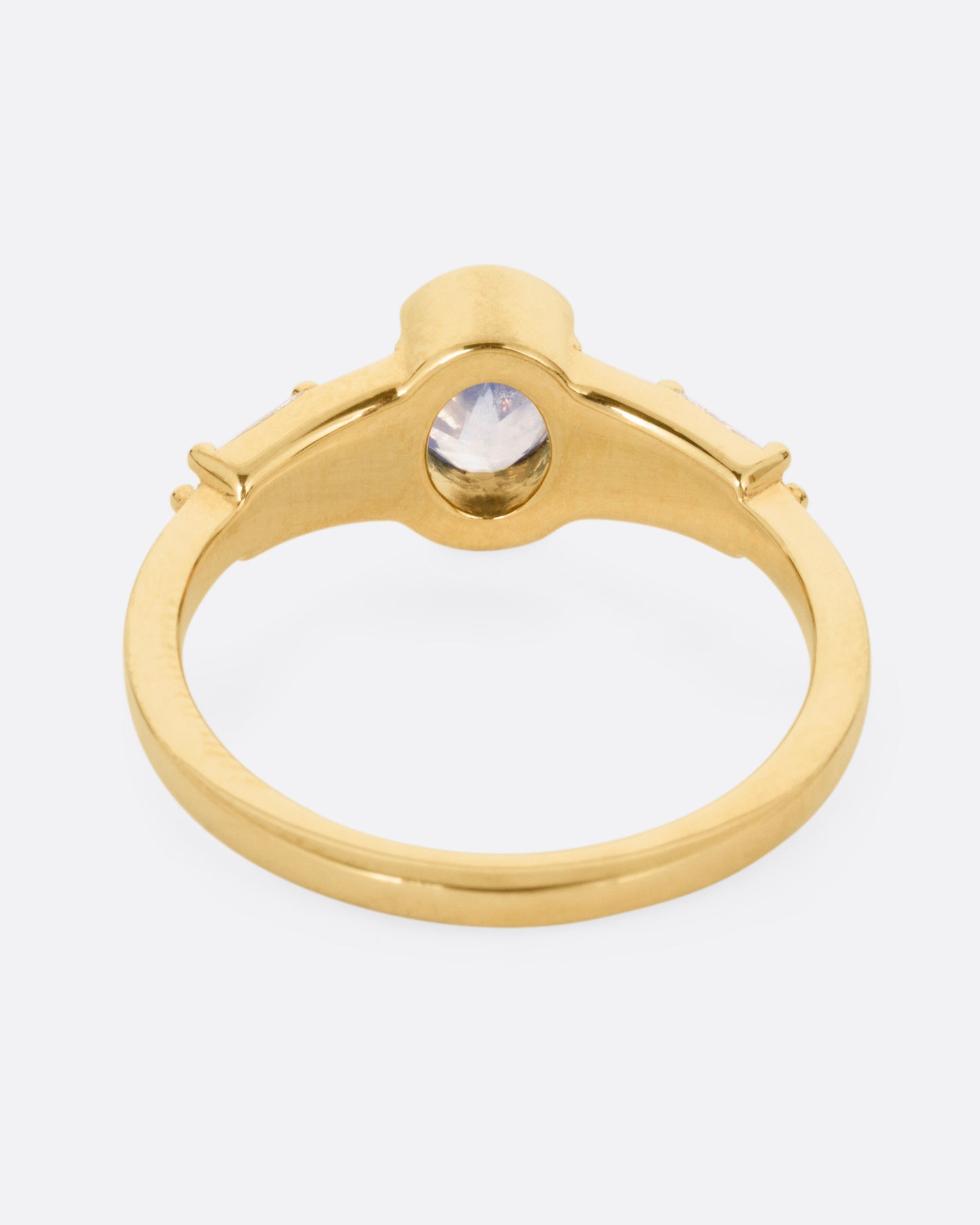 A yellow gold ring with stacked baguette diamonds and a bezel set sapphire, shown from the back.