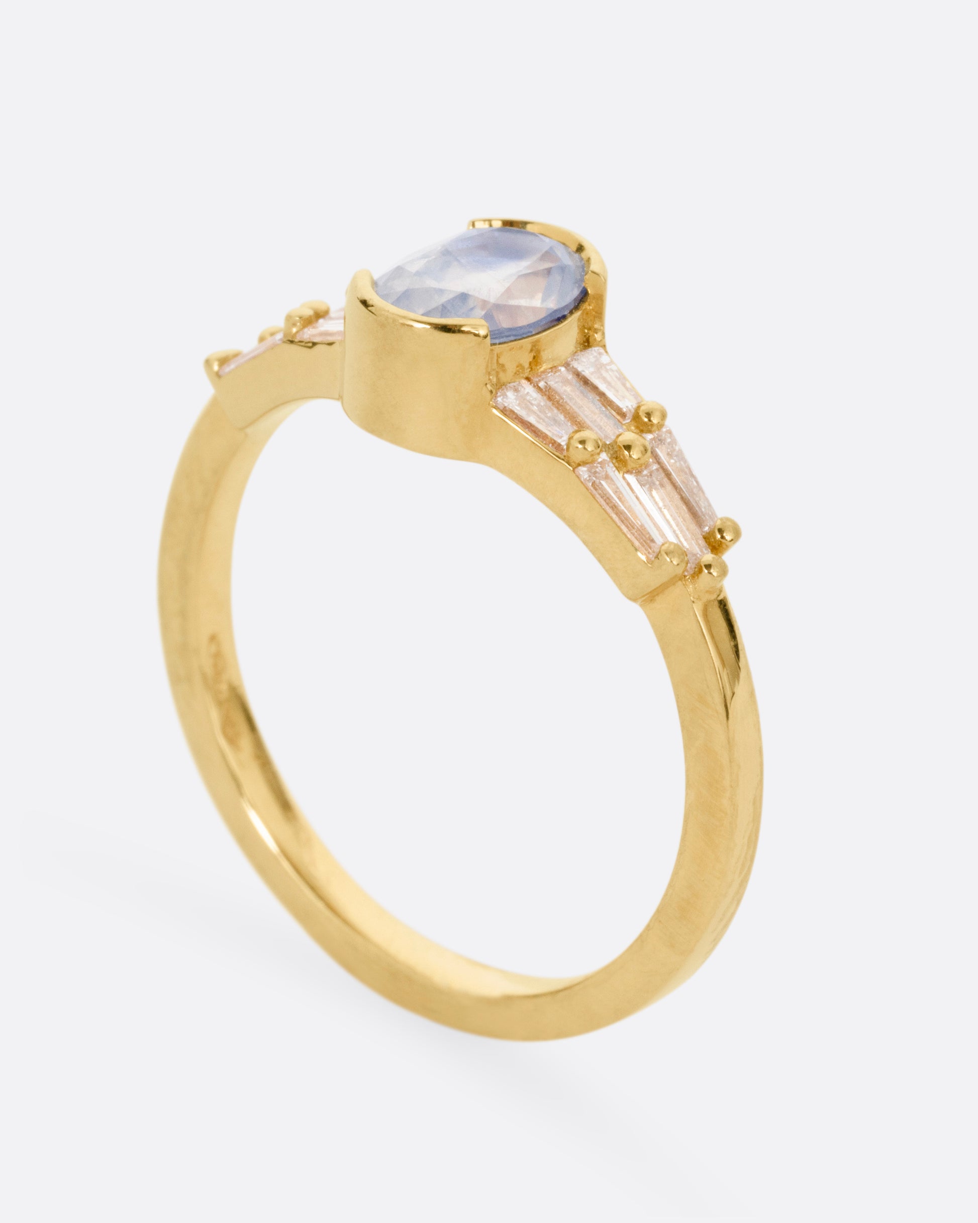 A yellow gold ring with stacked baguette diamonds and a bezel set sapphire, shown from the side standing up.