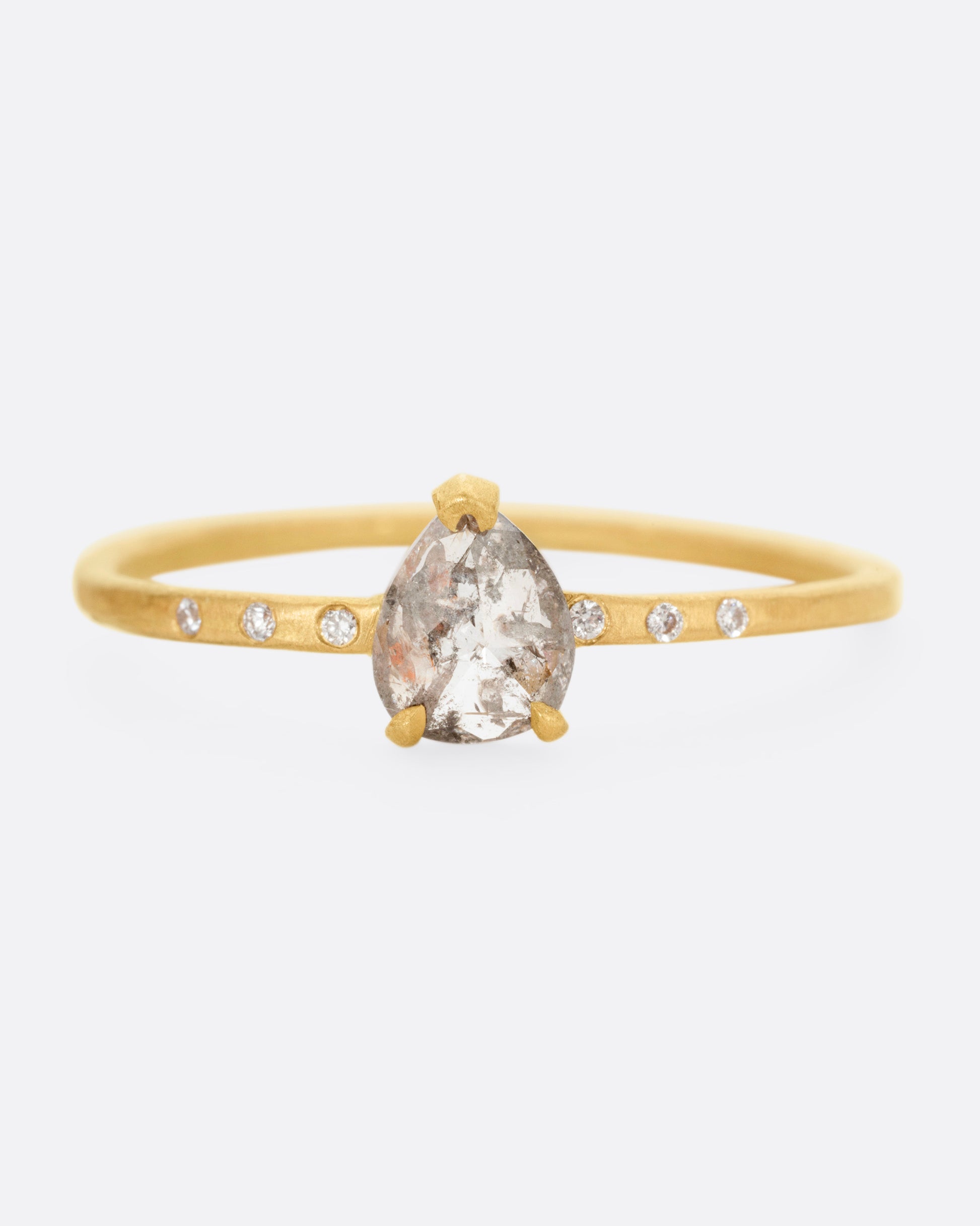 A yellow gold ring with a prong set salt and pepper diamond, flanked by tiny white diamond accents. Shown from the front.