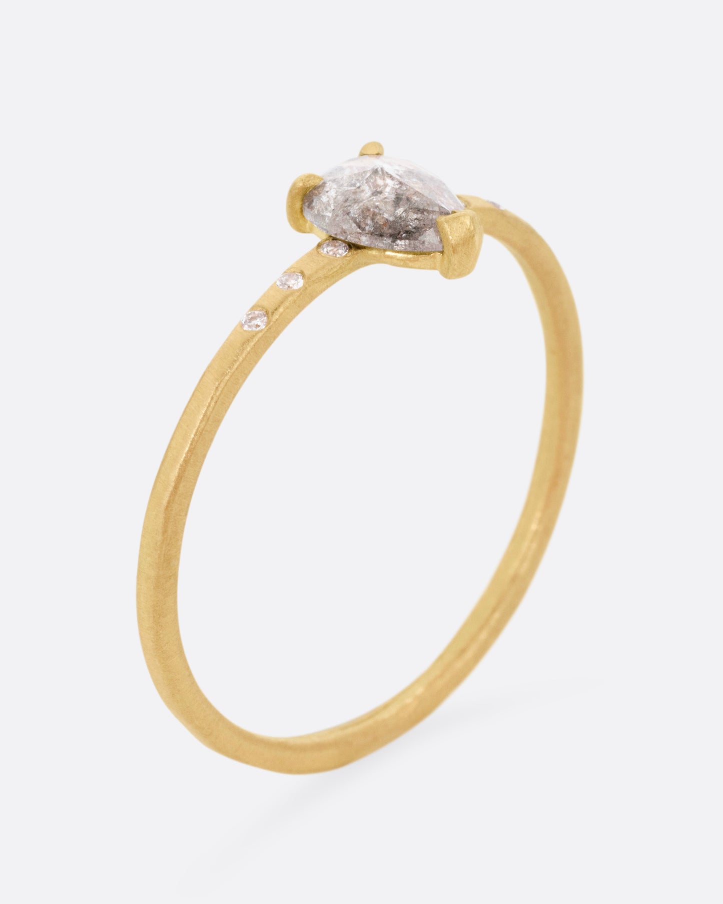 A yellow gold ring with a prong set salt and pepper diamond, flanked by tiny white diamond accents. Shown from the side standing up.