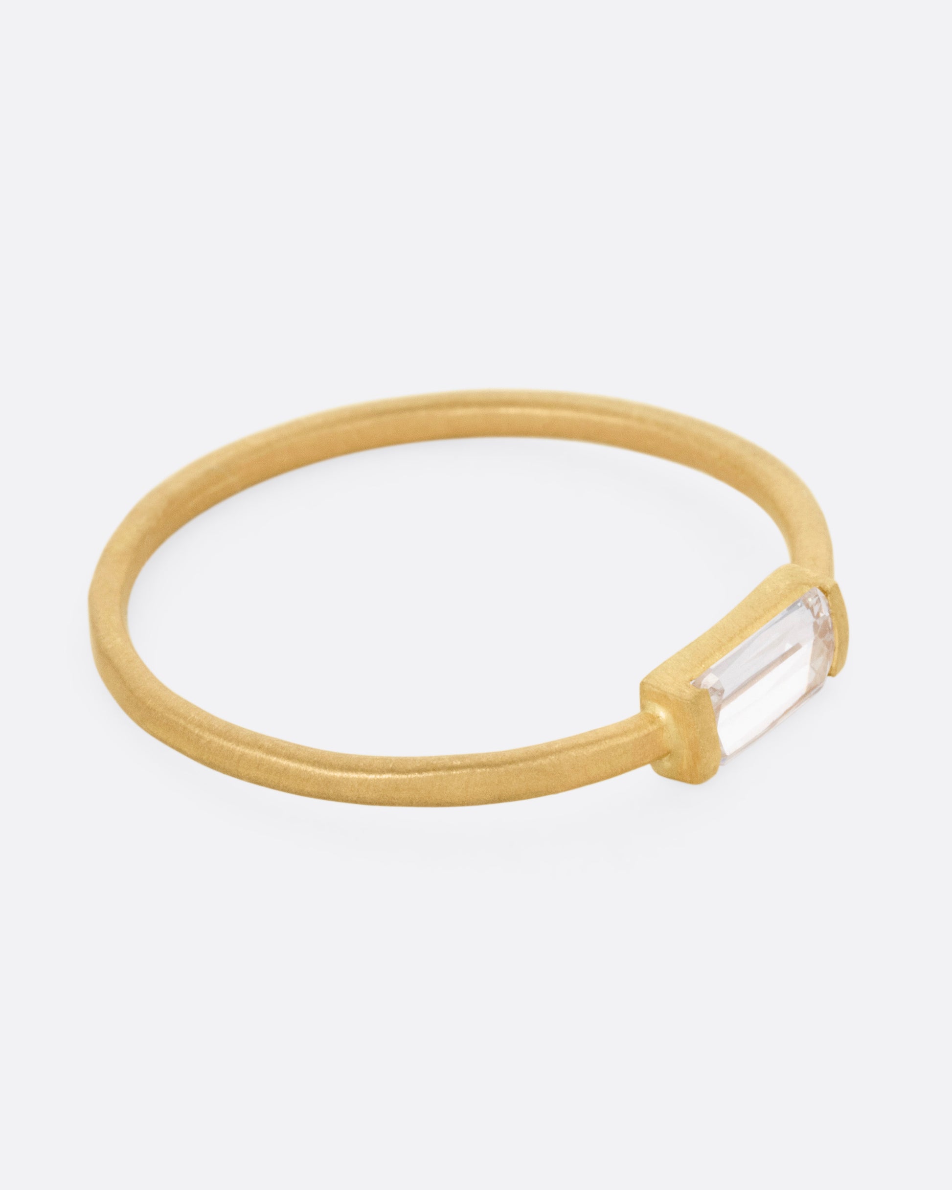 A yellow gold ring with a grey baguette diamond, shown from the side.