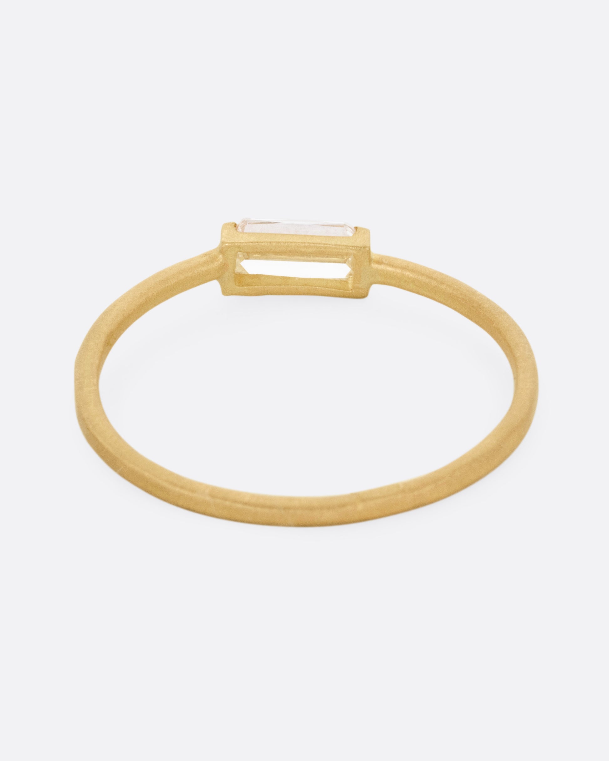 A yellow gold ring with a grey baguette diamond, shown from the back.
