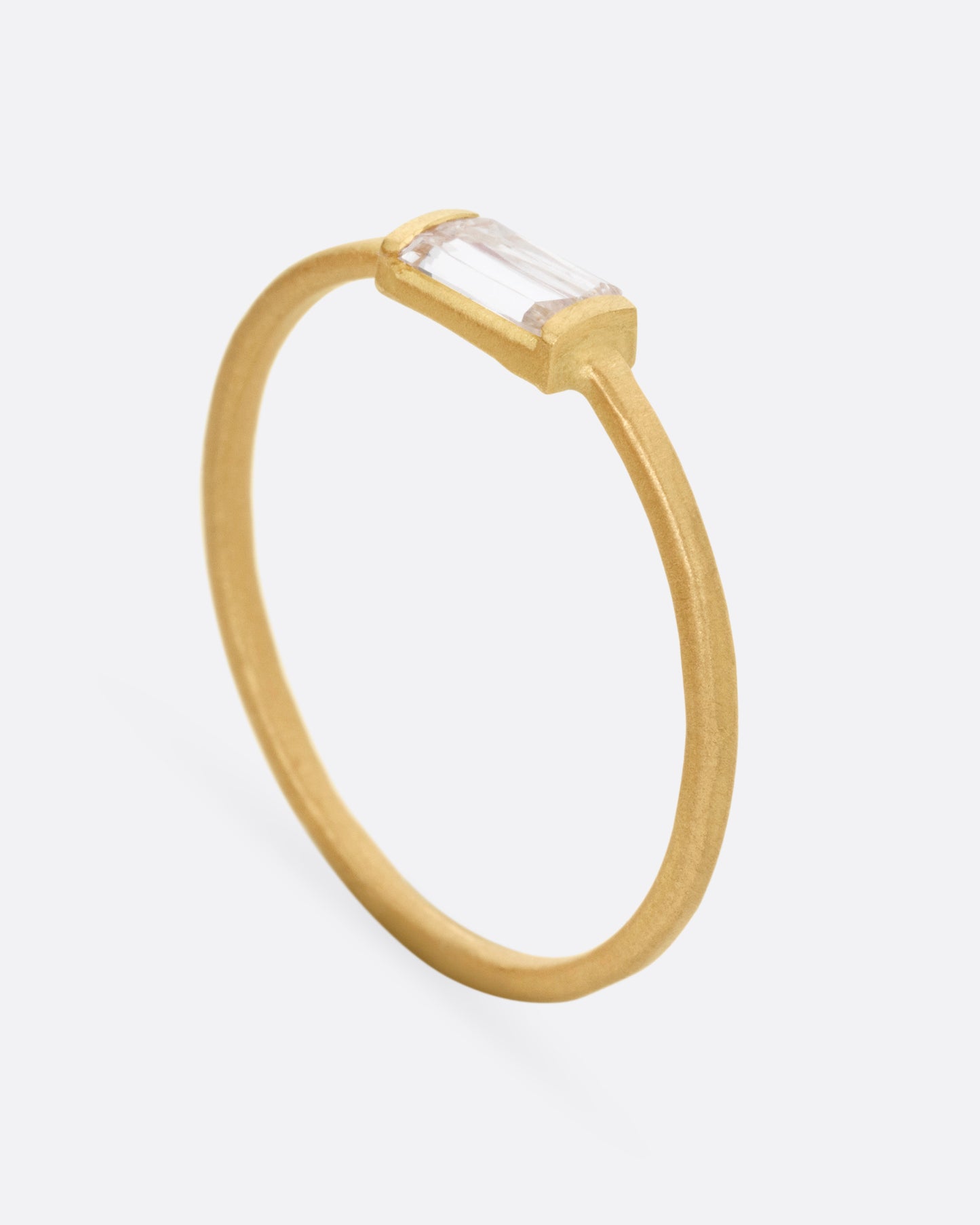 A yellow gold ring with a grey baguette diamond, shown from the side standing up.