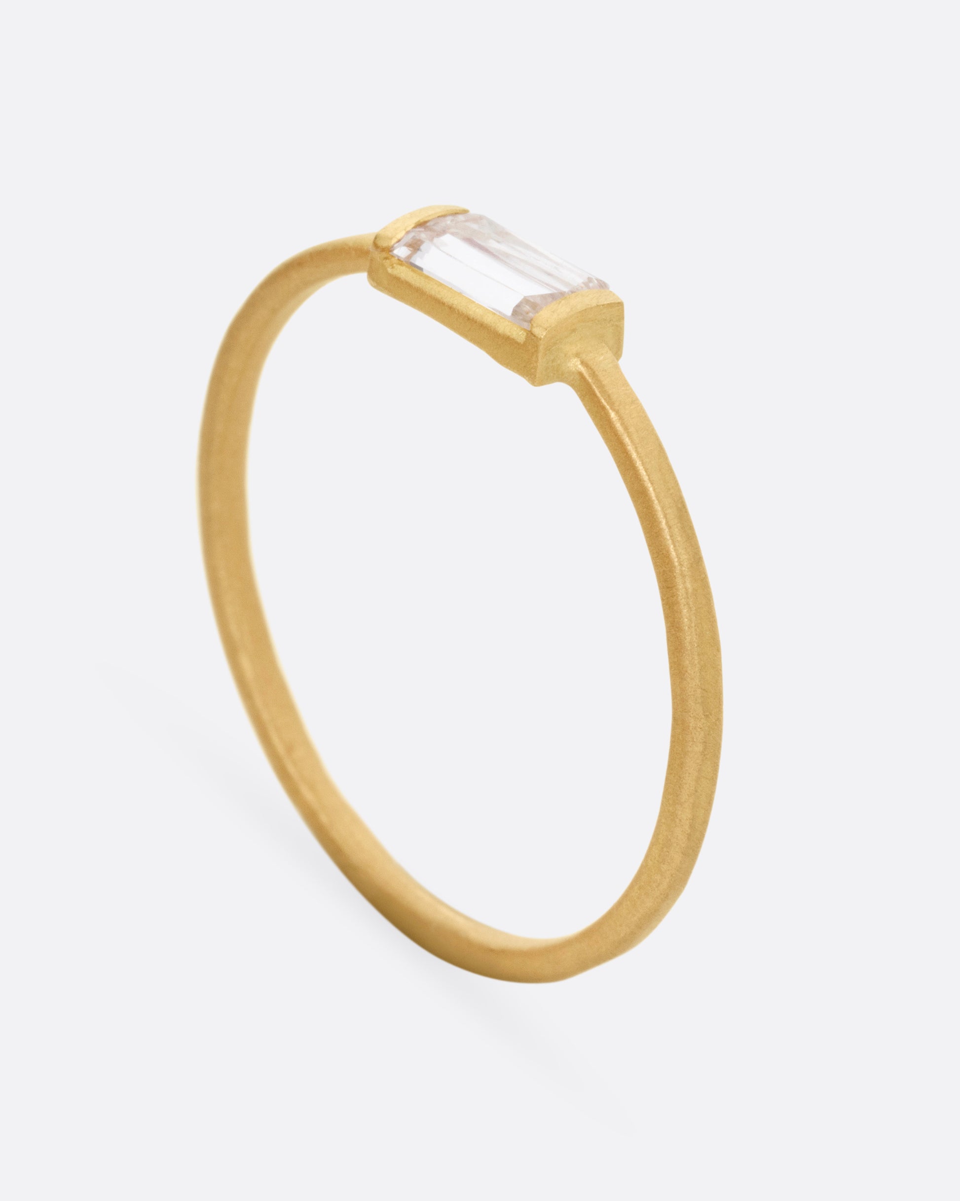A yellow gold ring with a grey baguette diamond, shown from the side standing up.