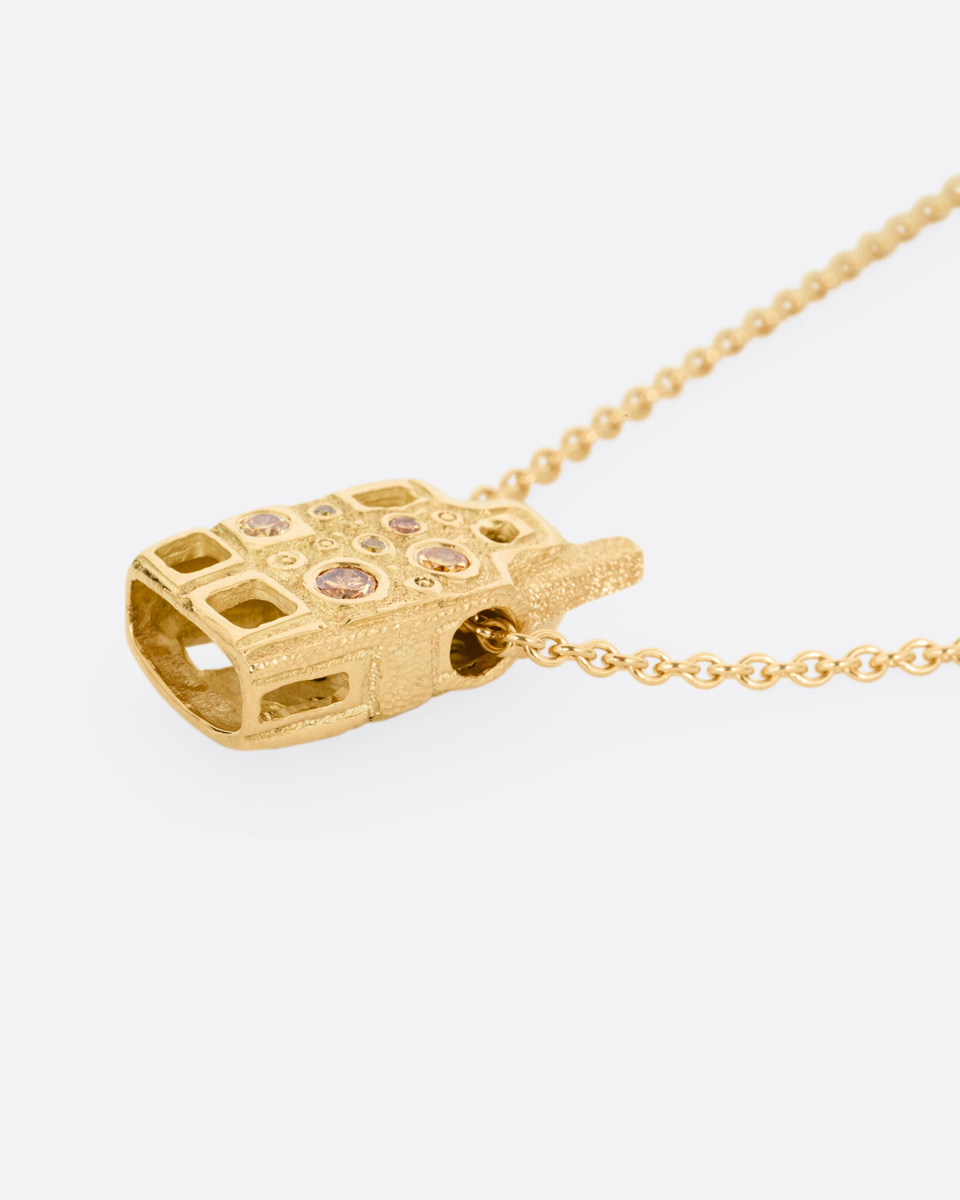 A yellow gold house-shaped pendant with multi-colored diamonds, on a cable chain, shown lying flat from the side. 