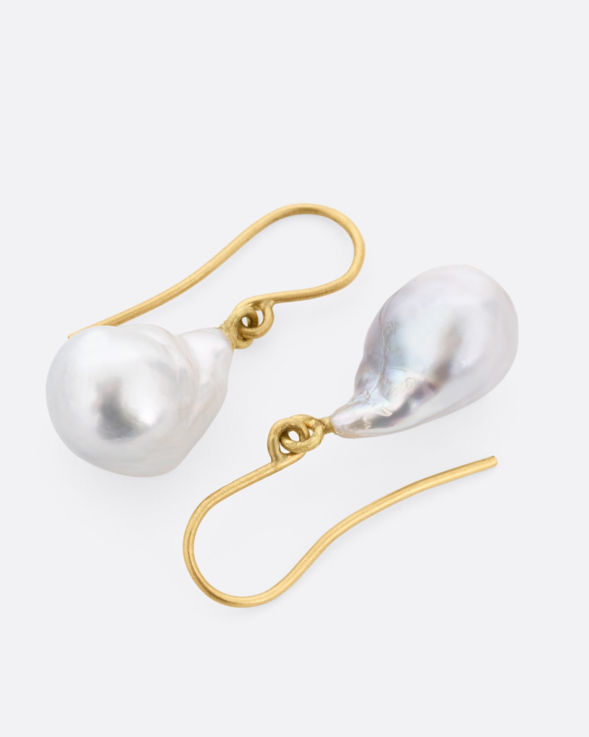 A pair of pearl earrings with yellow gold ear hooks, shown lying on their sides.