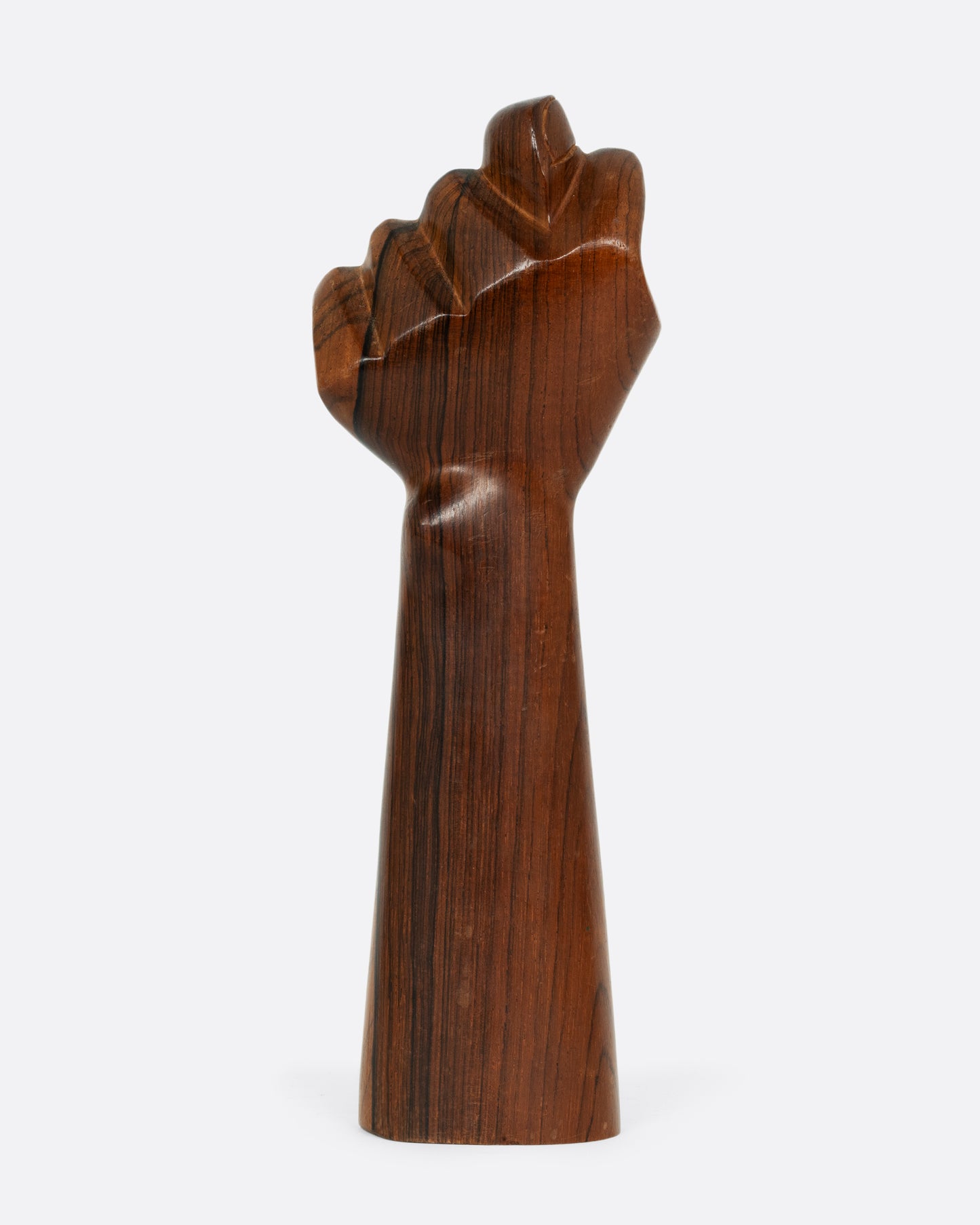 A carved wooden hand with the thumb crossed between the index and middle fingers in a fist. Shown from the back.