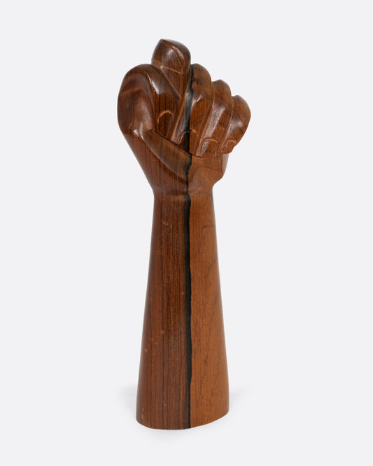 A carved wooden hand with the thumb crossed between the index and middle fingers in a fist. Shown from the front.