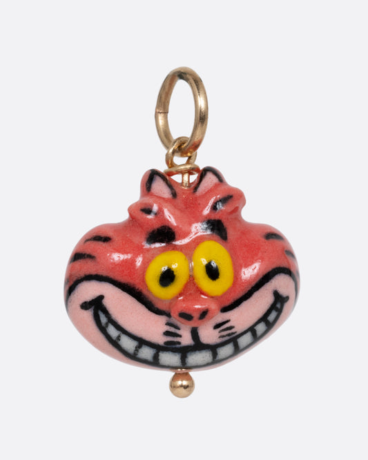 A porcelain cheshire cat charm with a yellow gold bail. Shown from the front.