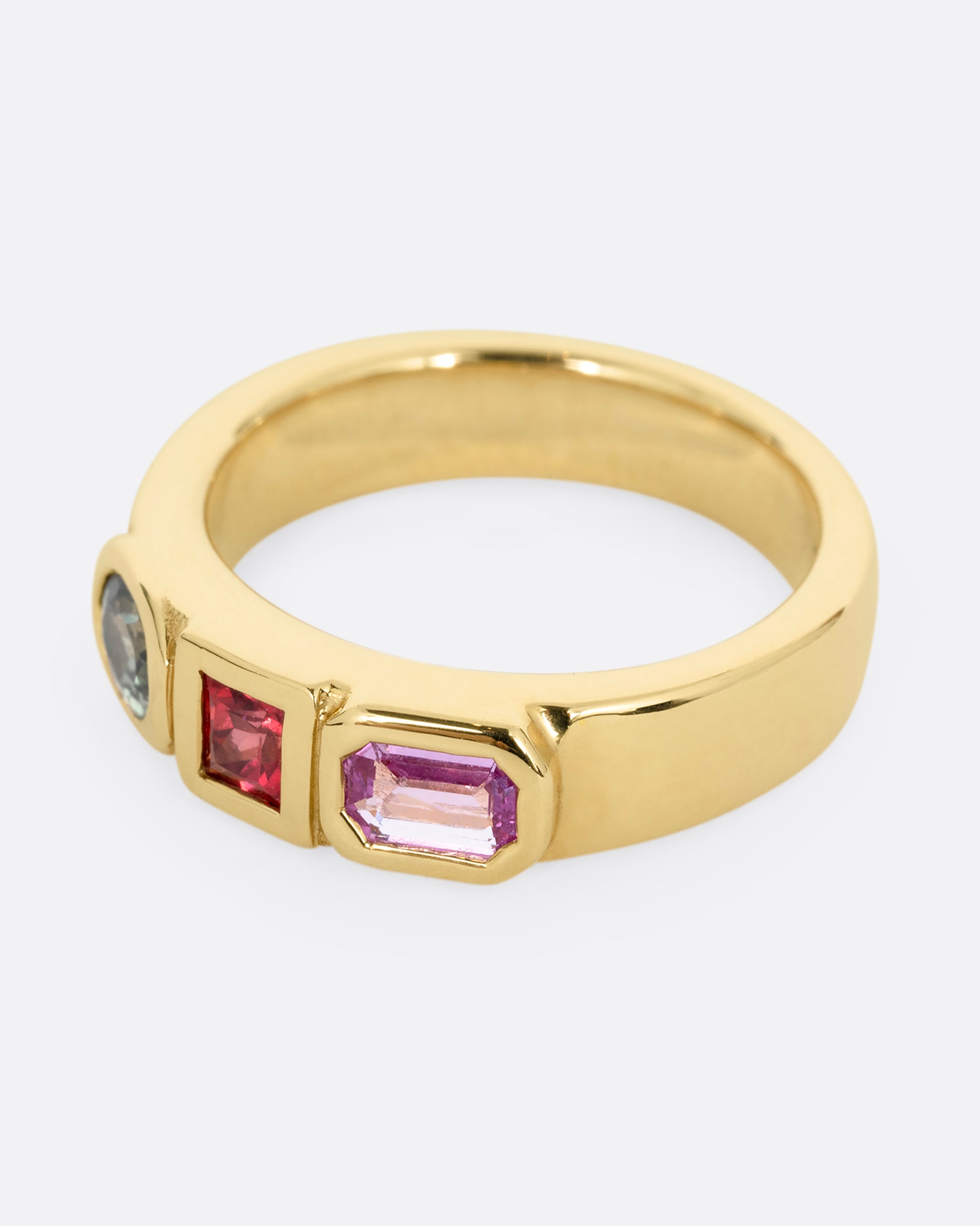 A yellow gold band with three mixed cut multicolored sapphires. Shown from the side.