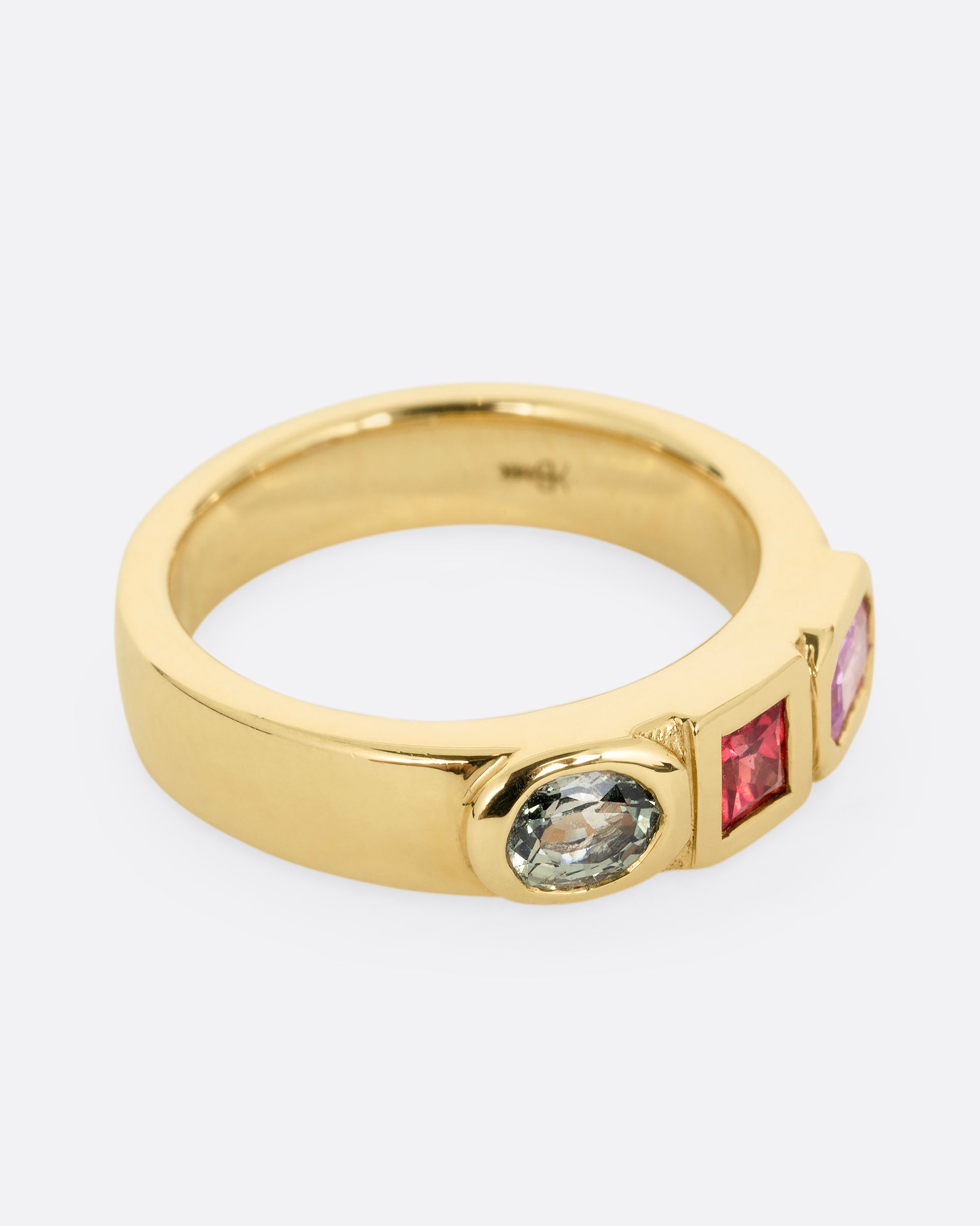 A yellow gold band with three mixed cut multicolored sapphires. Shown from the side.