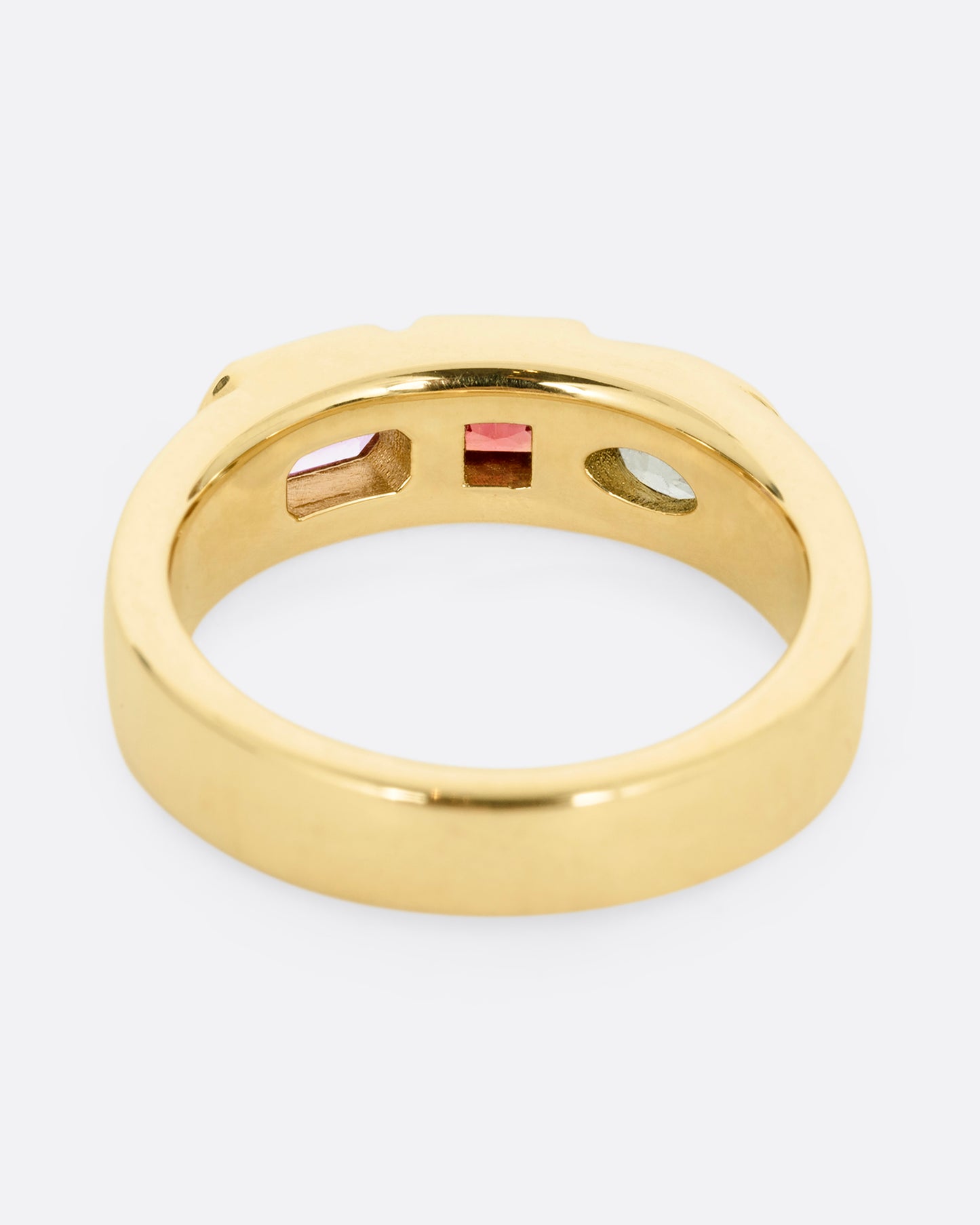 A yellow gold band with three mixed cut multicolored sapphires. Shown from the back.
