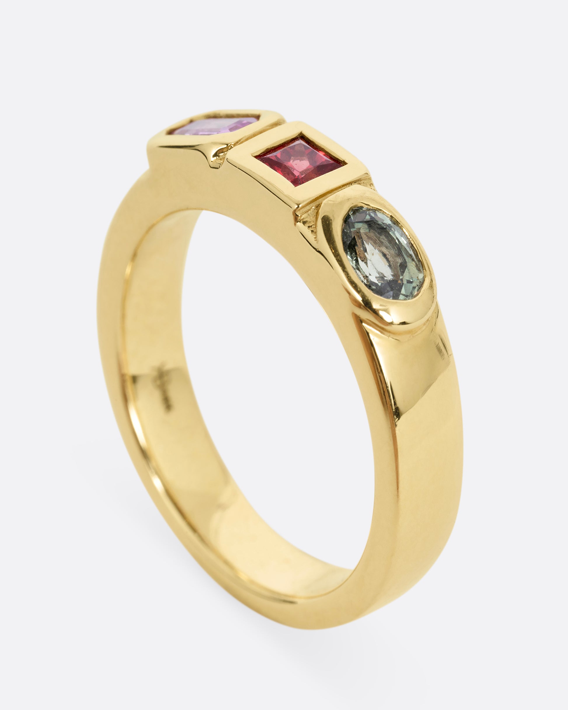 A yellow gold band with three mixed cut multicolored sapphires. Shown from the side standing up.
