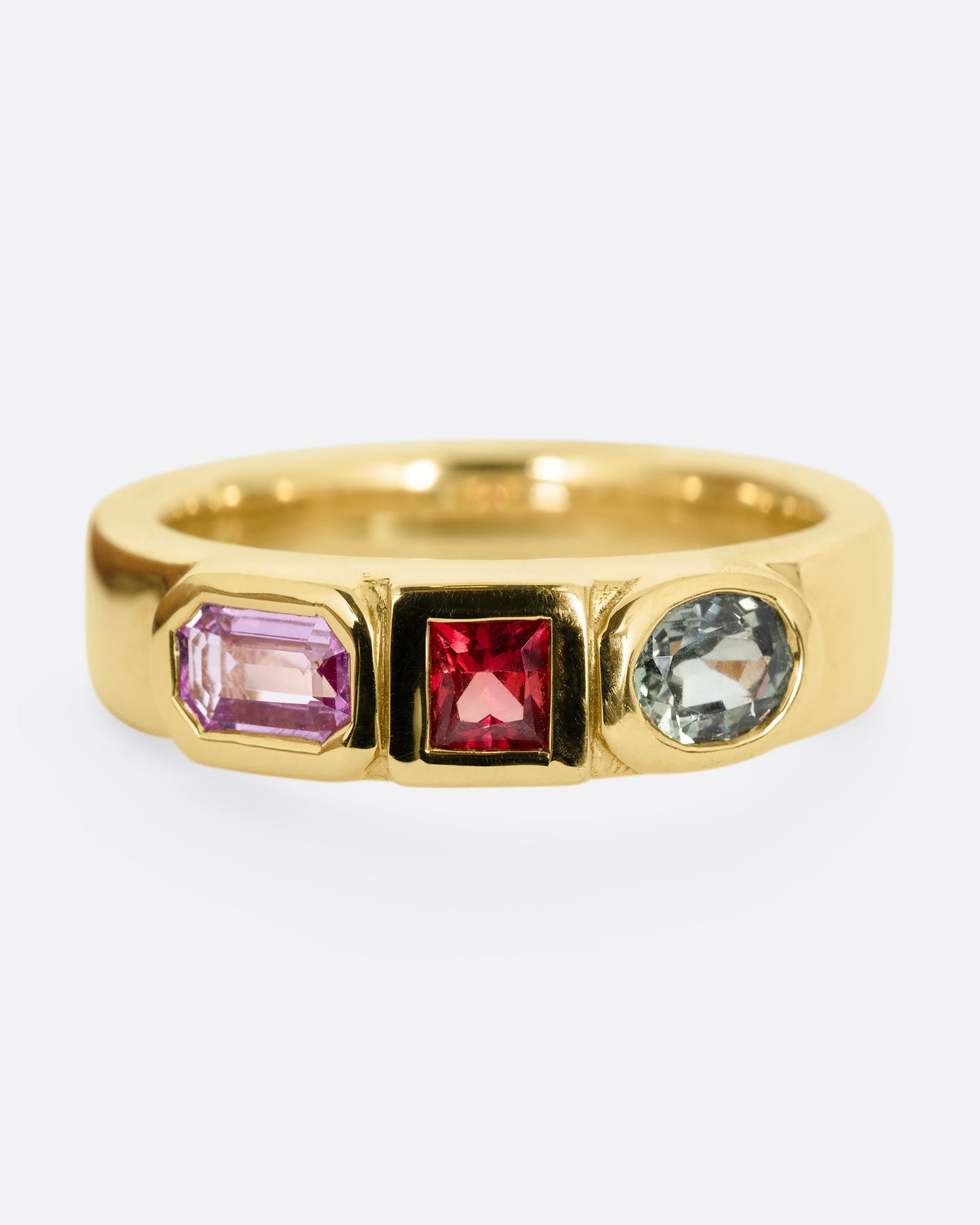 A yellow gold band with three mixed cut multicolored sapphires. Shown from the front.