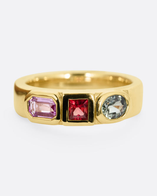 A yellow gold band with three mixed cut multicolored sapphires. Shown from the front.
