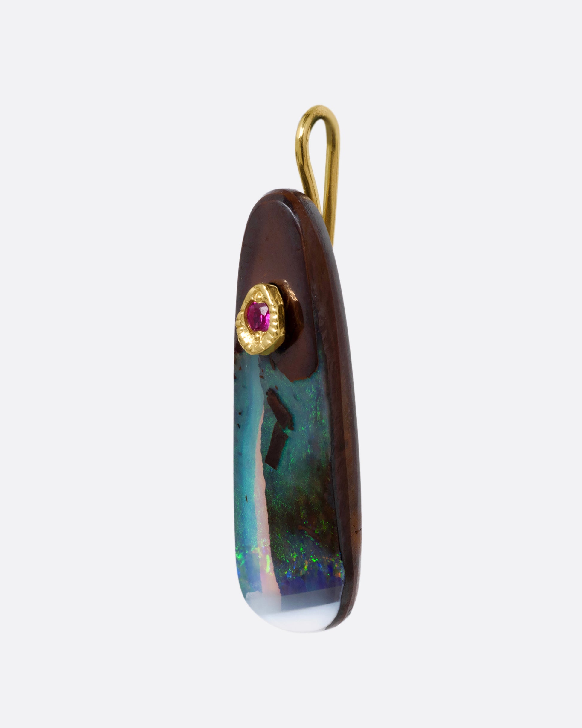 A free-form boulder opal charm topped with a yellow gold bail with a pink sapphire at its center. Shown from the side.