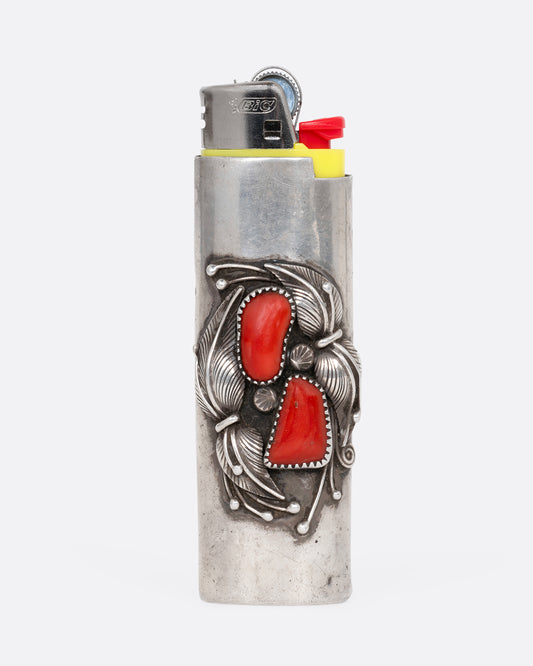 A sterling silver lighter with feather motif hugging two pieces of coral, shown from the front holding a yellow contemporary lighter.