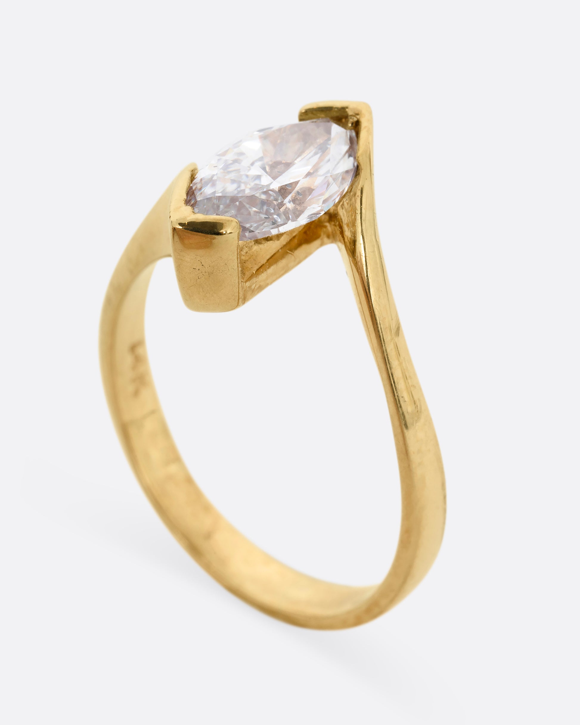 A yellow gold ring with a marquis diamond at the center. Shown from the side, standing up.